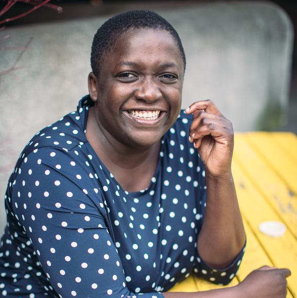 Smiling woman with short hair wearing a blue polka dot shirt, sitting outdoors.