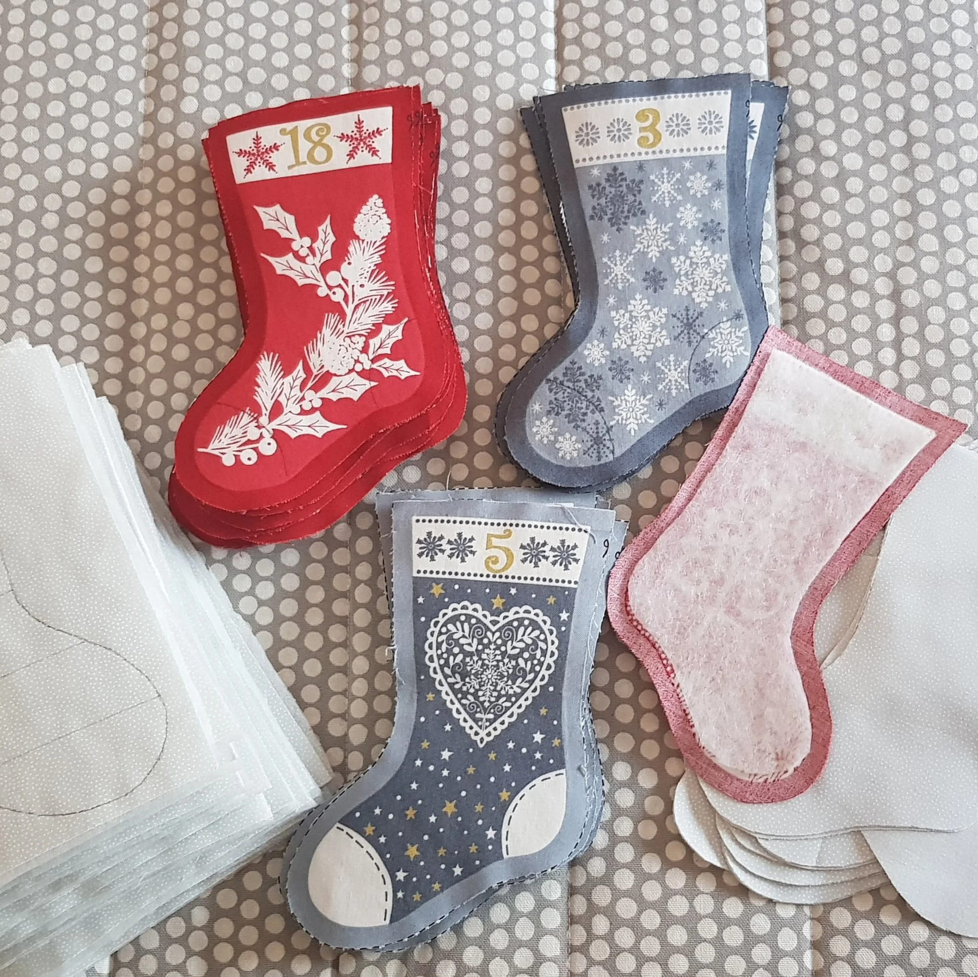 Holiday paper stockings with numbers 18, 3, and 5 printed on them, surrounded by stacks of white napkins on polka dot fabric.