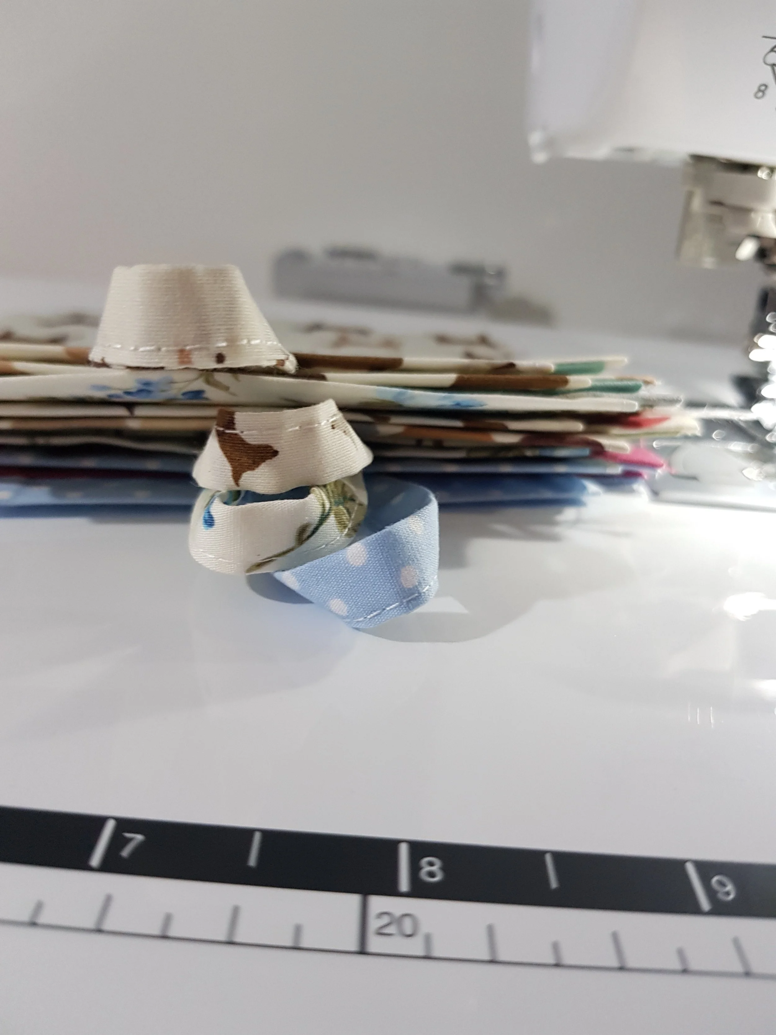 Close-up of fabric-covered hair rollers and a stack of papers or magazines on a white surface, with part of a clock or measuring device in the foreground.
