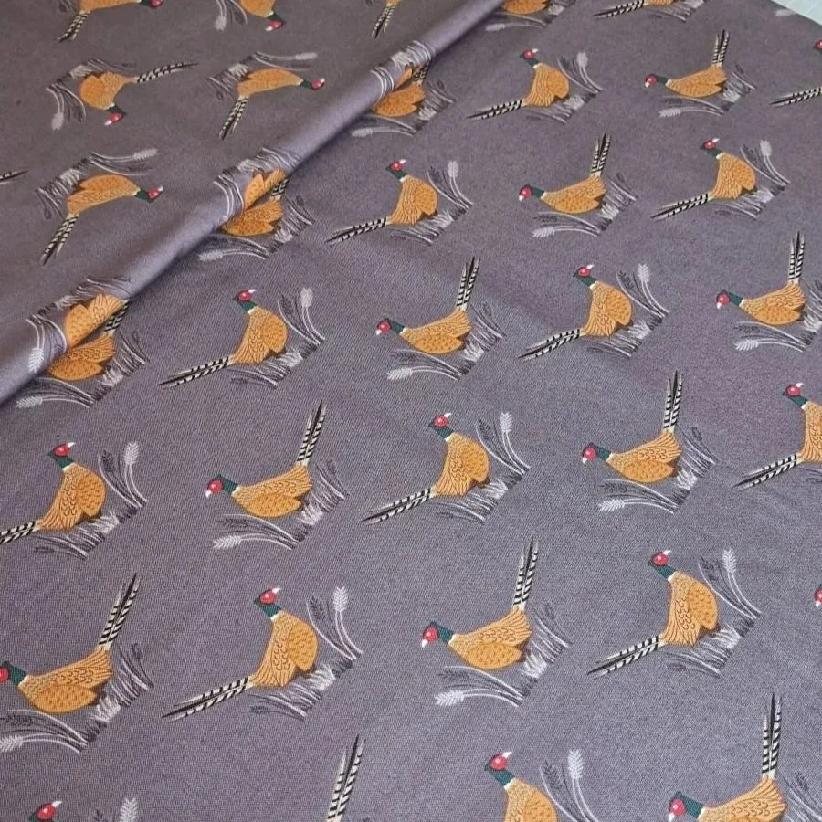 Dark purple cotton fabric with pattern of birds in orange. View at unfolded fabric from a bolt
