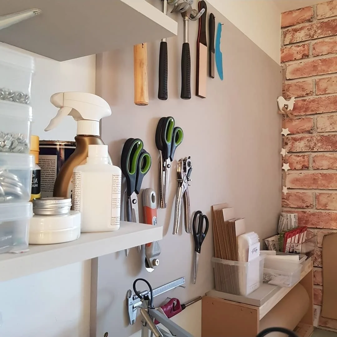 Organization of kitchen utensils, scissors, and tools hung on a wall, with containers of hardware and cleaning supplies on a shelf.