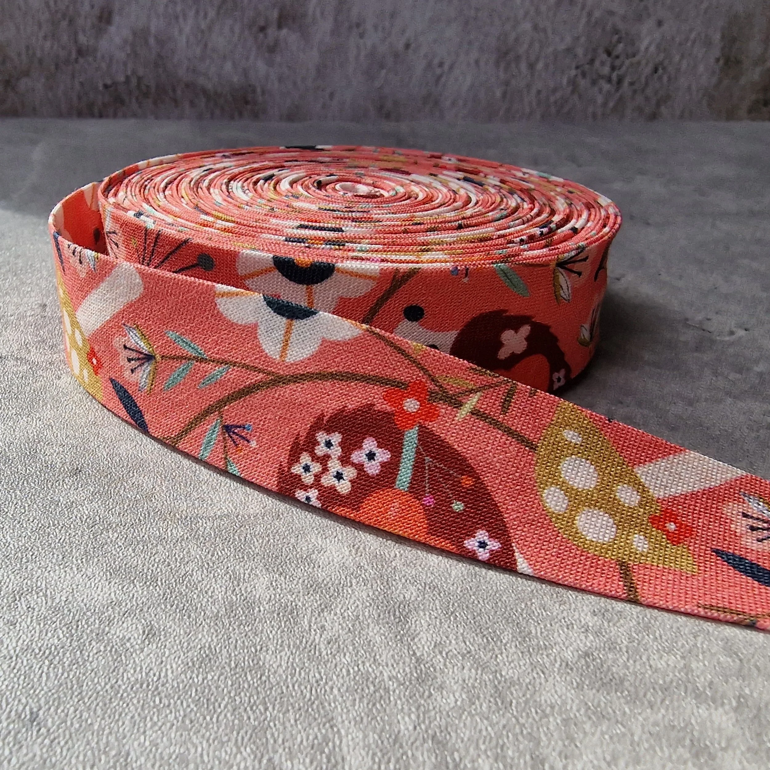 A rolled fabric ribbon with a pink floral pattern on a silver surface with a gray background.