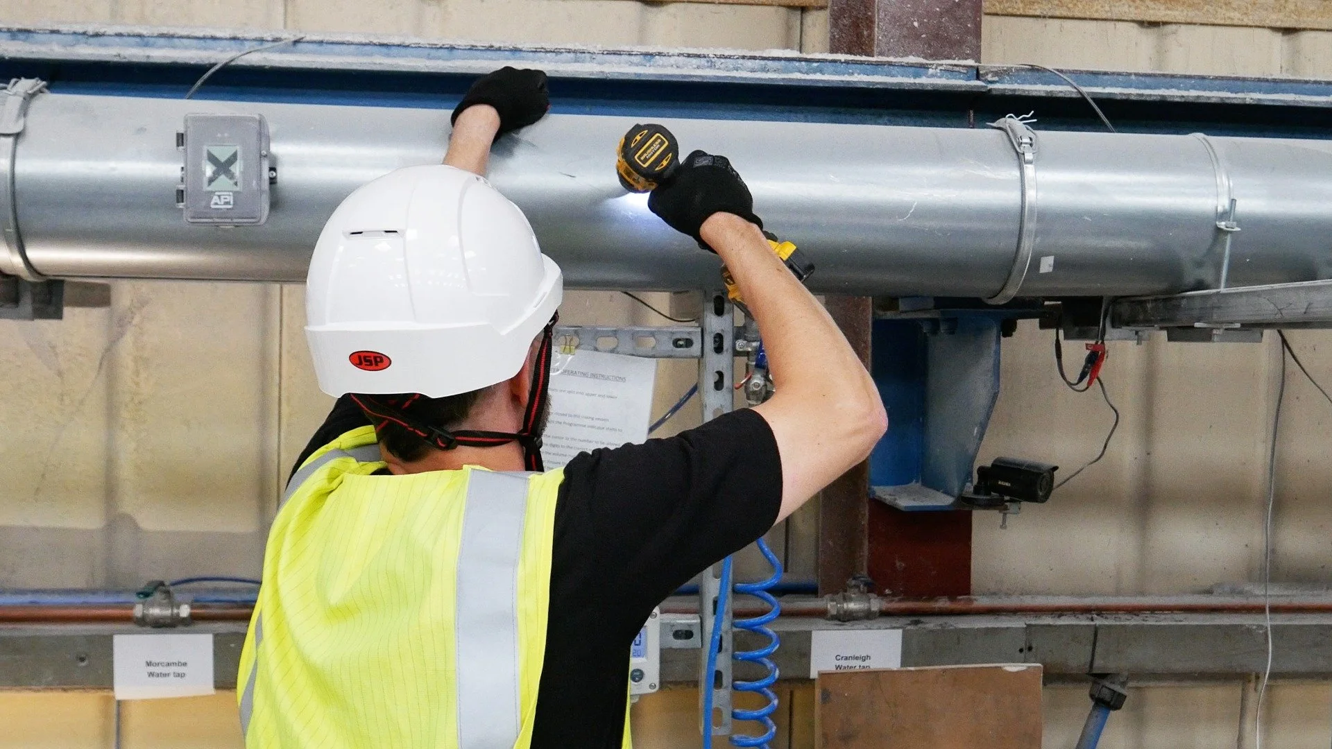 Engineer working on an overhead metal extraction duct with a cordless drill