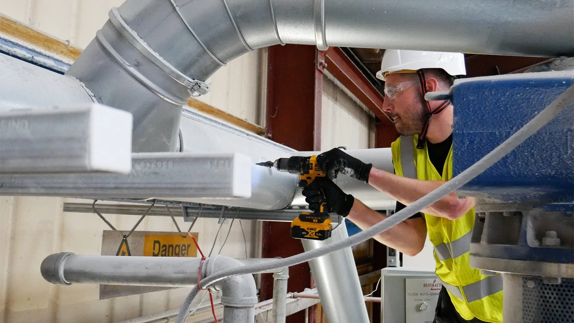 Engineer working on metal extraction ductwork with a cordless drill