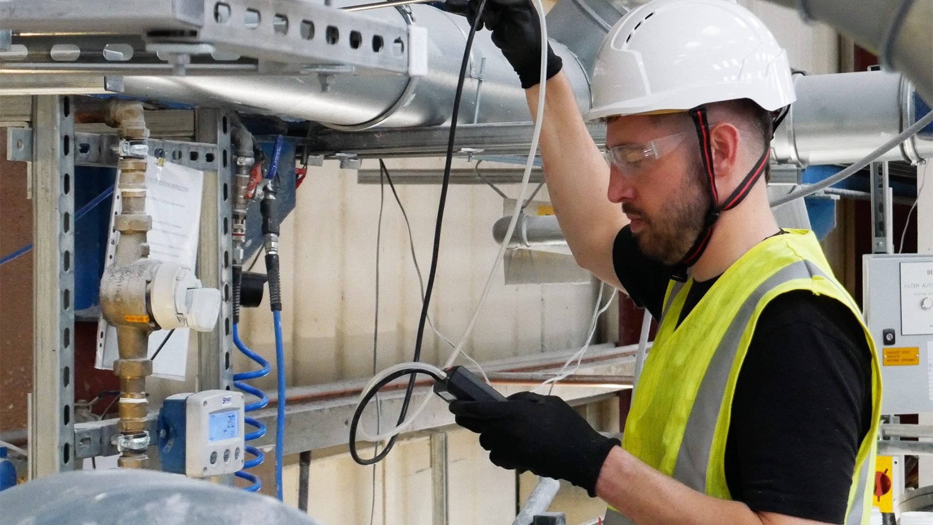 Engineer measuring extraction performance with a handheld instrument beside industrial ductwork