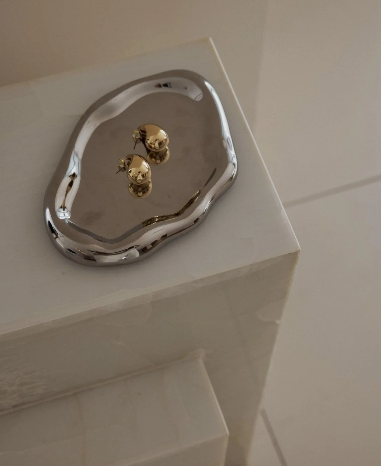 A decorative silver tray with gold-colored bell earrings placed on it, sitting on a white surface.