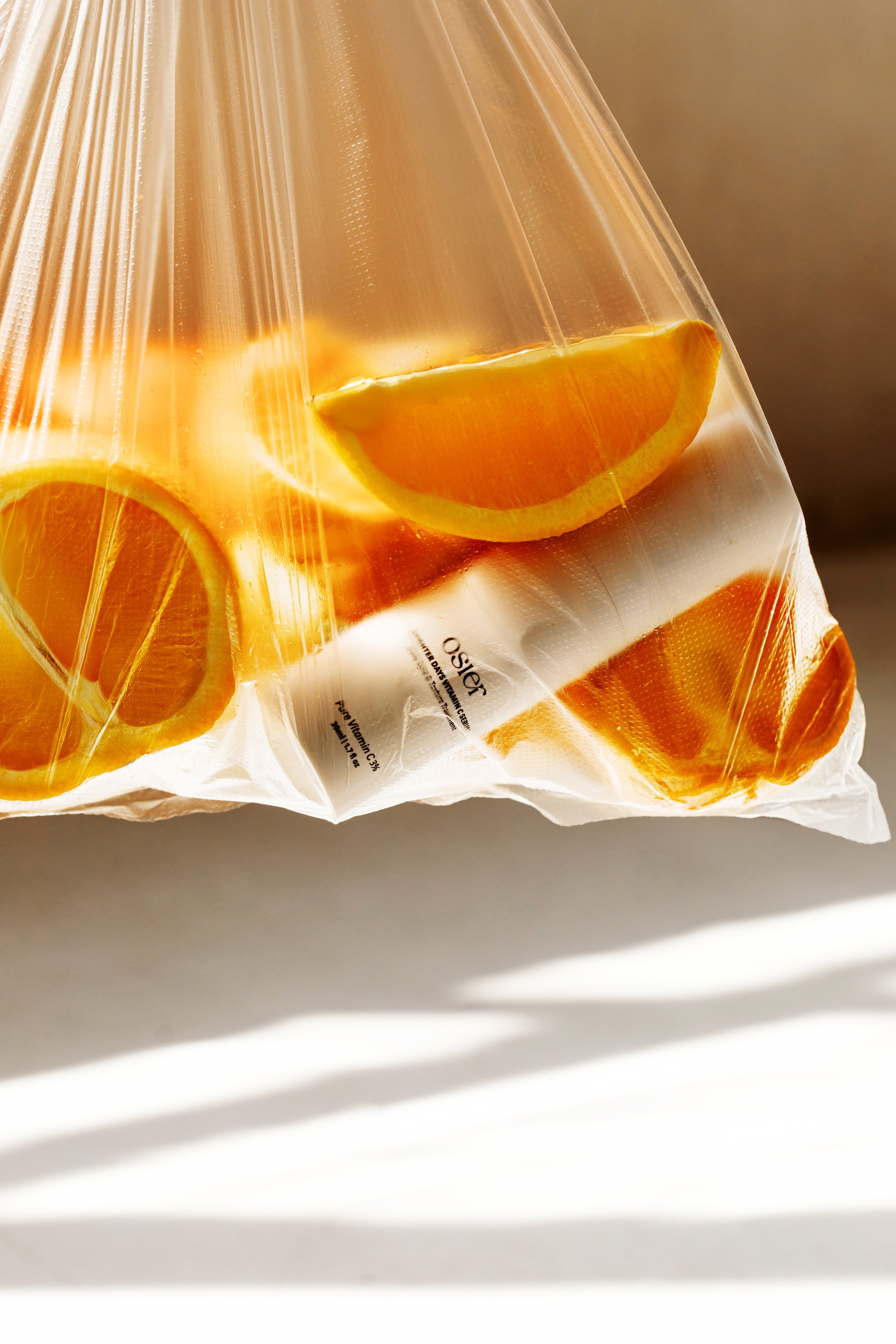 Clear plastic bag containing sliced oranges, with sunlight creating shadows on a white surface.