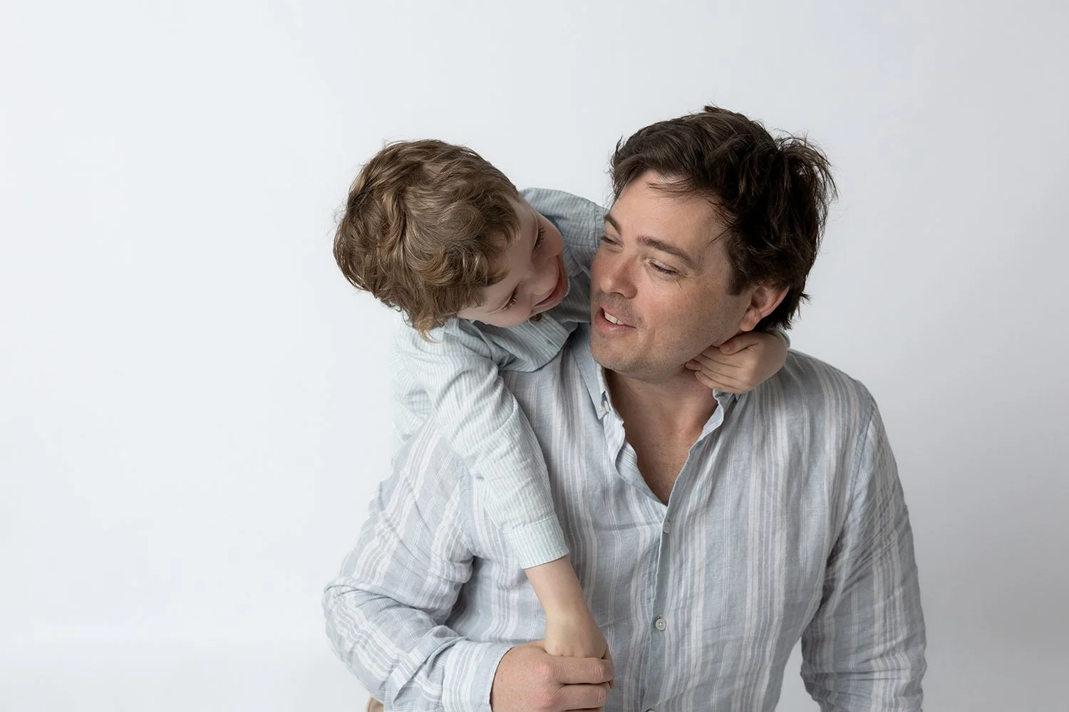A man giving a piggyback ride to a young boy, both smiling and enjoying a playful moment against a plain white background.