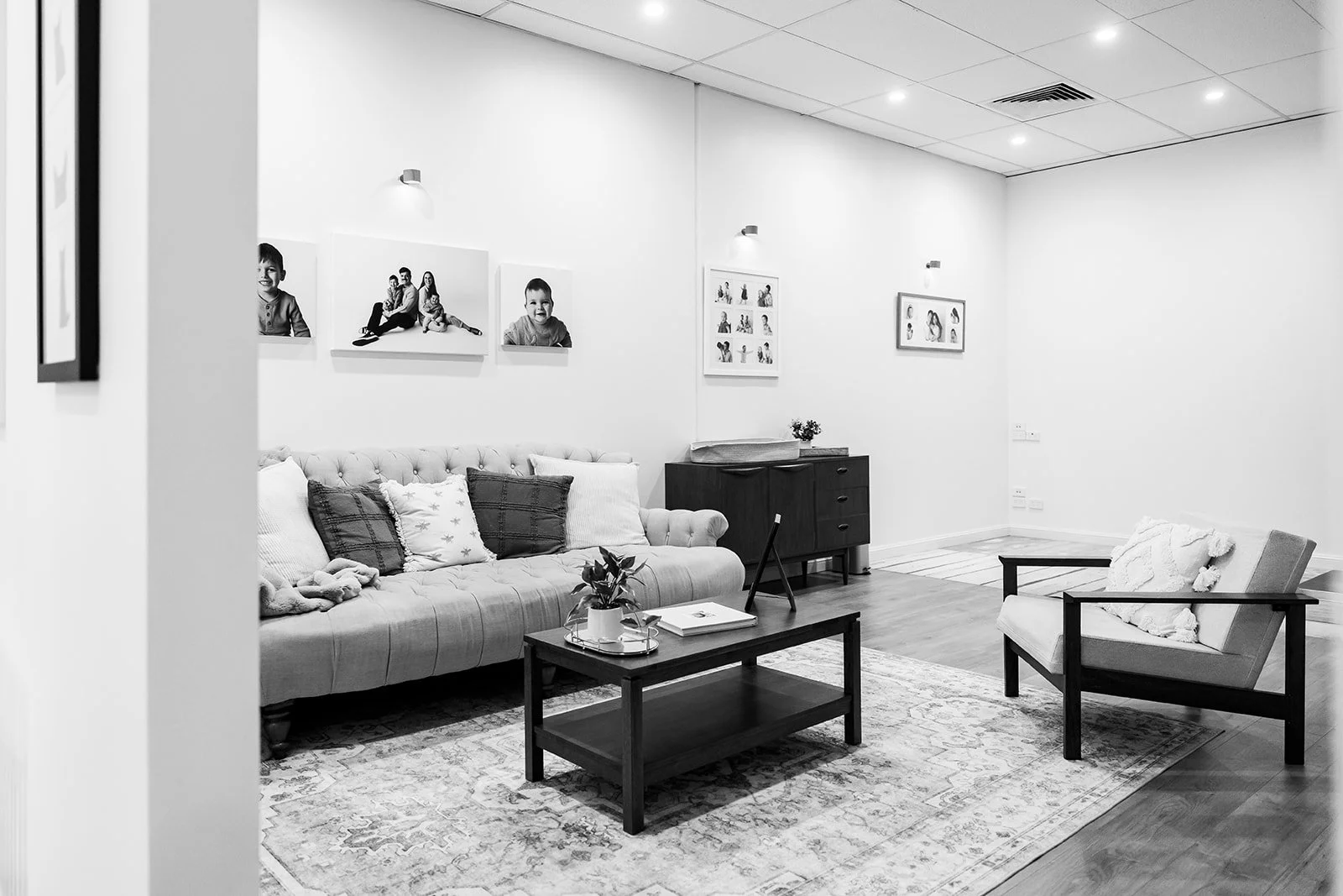 A modern living room styled photography studio with a tufted sofa, armchair, wooden coffee table, rug, wall art, and simple decor in black and white.