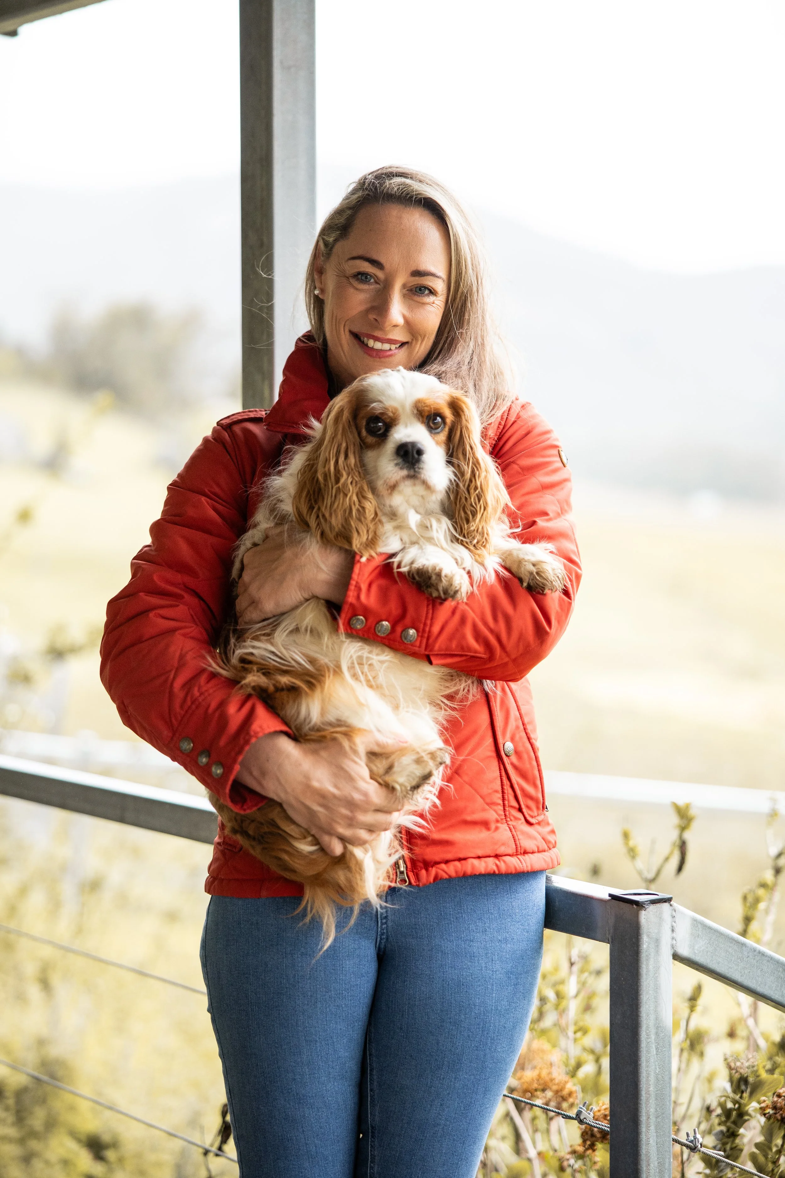 Alex Pope holding a Cavalier King Charles Spaniel on a balcony with a blurred outdoor landscape in the background - Organisational culture consultant Australia
