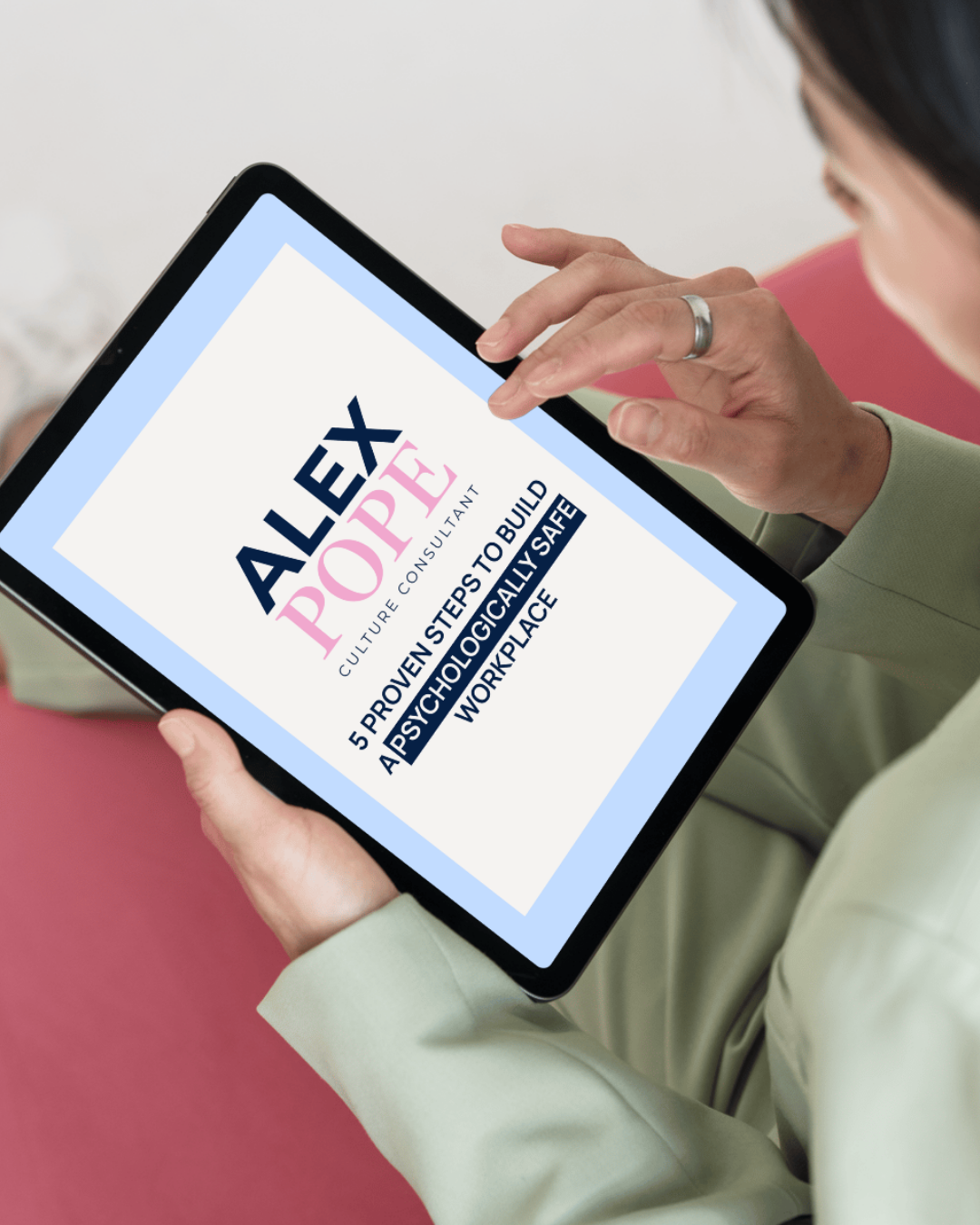 Person holding a tablet displaying a website about building a psychologically safe workplace, with the headline 'Alex Pope Culture Consultant' and the subtitle '5 Proven Steps to Build a Psychologically Safe Workplace'.