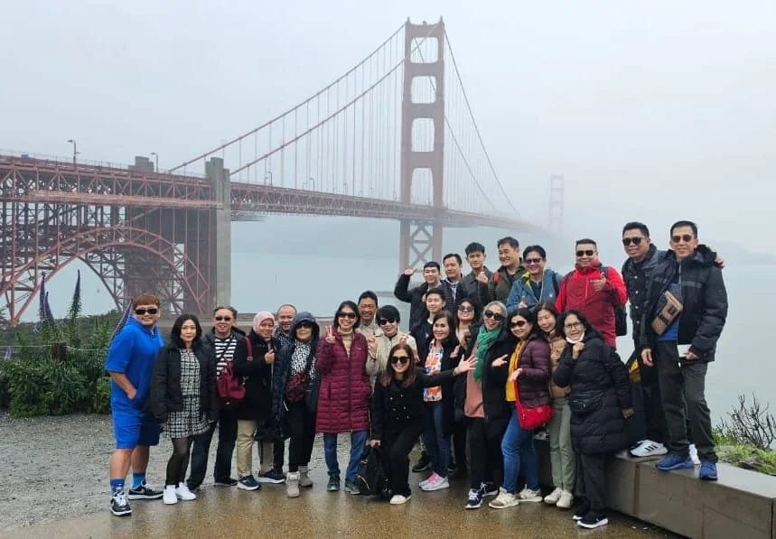 Group of people posing in front of the Golden Gate Bridge in foggy weather.