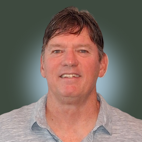 A man with brown hair, wearing a light grey collared shirt, smiling against a green background.