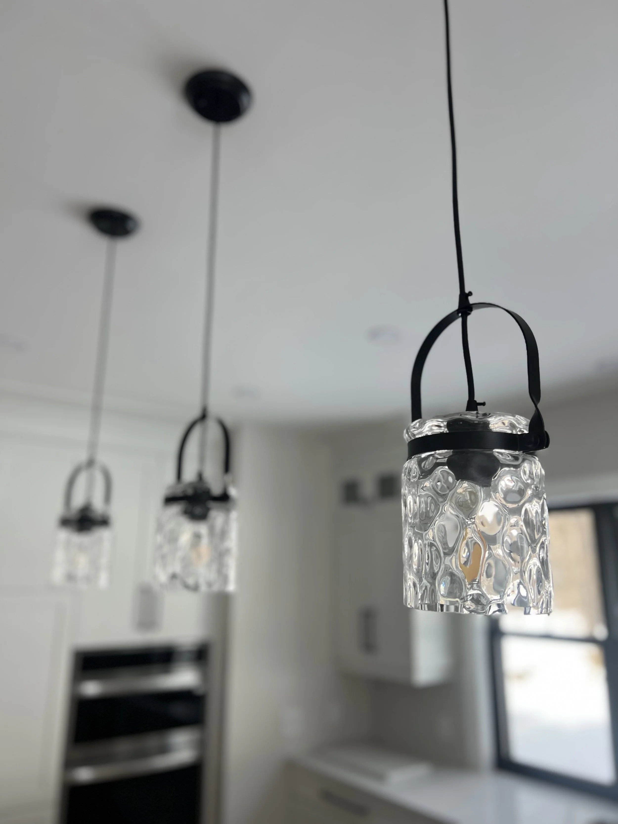 Three pendant lights with textured glass shades hanging from black cords in a modern kitchen.