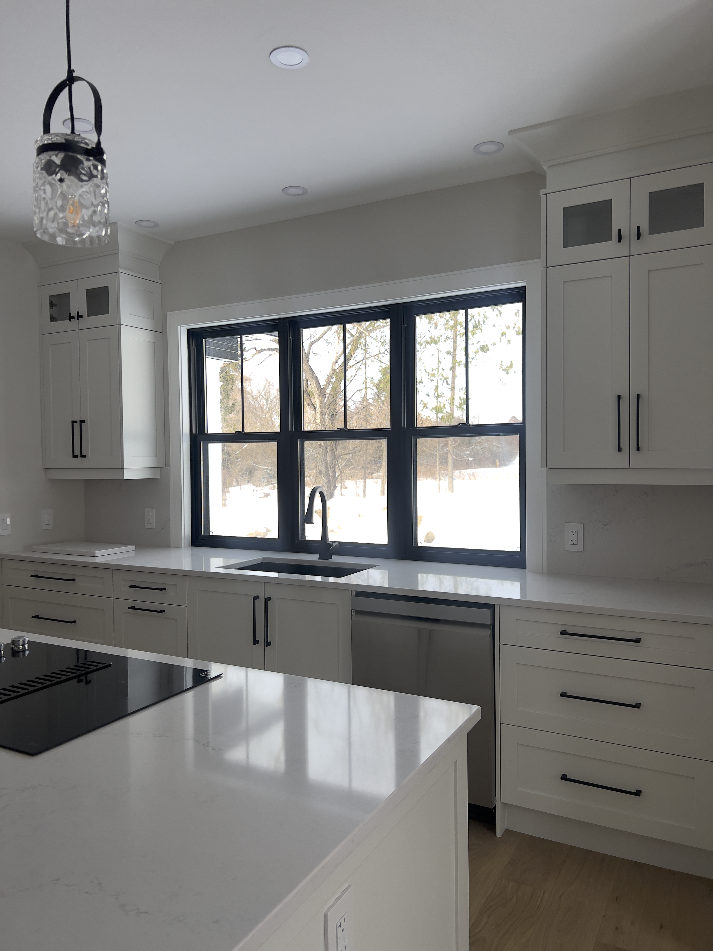 Modern kitchen with white cabinets, black hardware, marble countertops, black-framed windows, and a view of snowy outdoors.