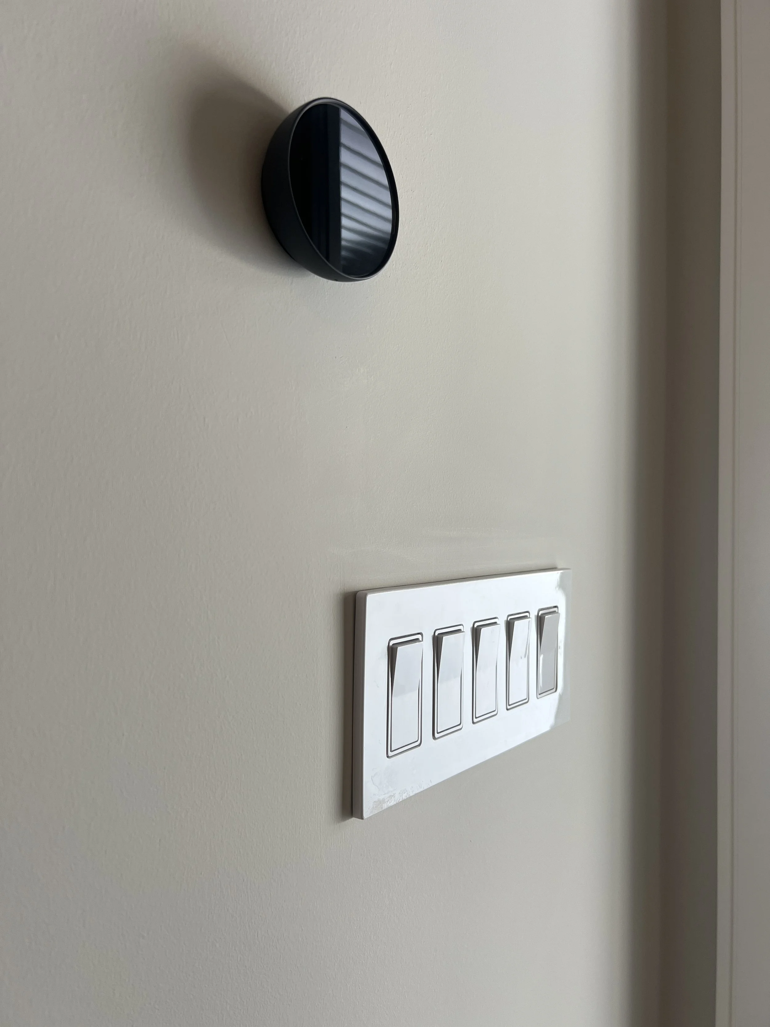 A black smart thermostat and a white multi-gang switch plate with four switches on a beige wall.