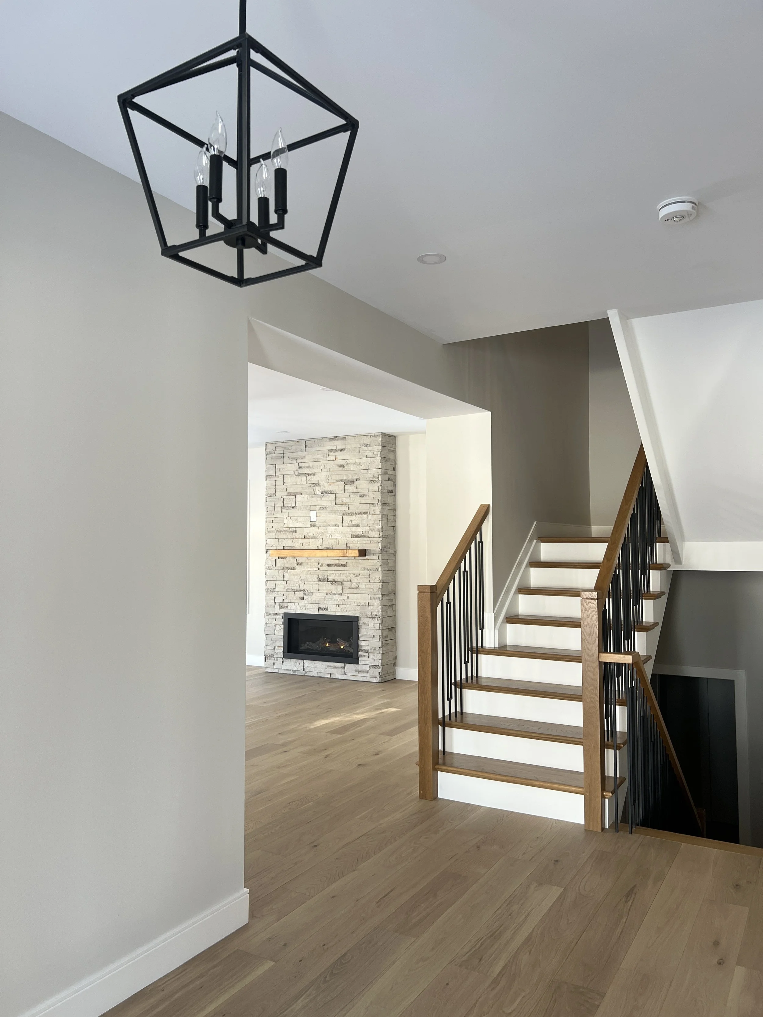 Interior view of a modern home with a staircase, a stone fireplace, and a black geometric chandelier.