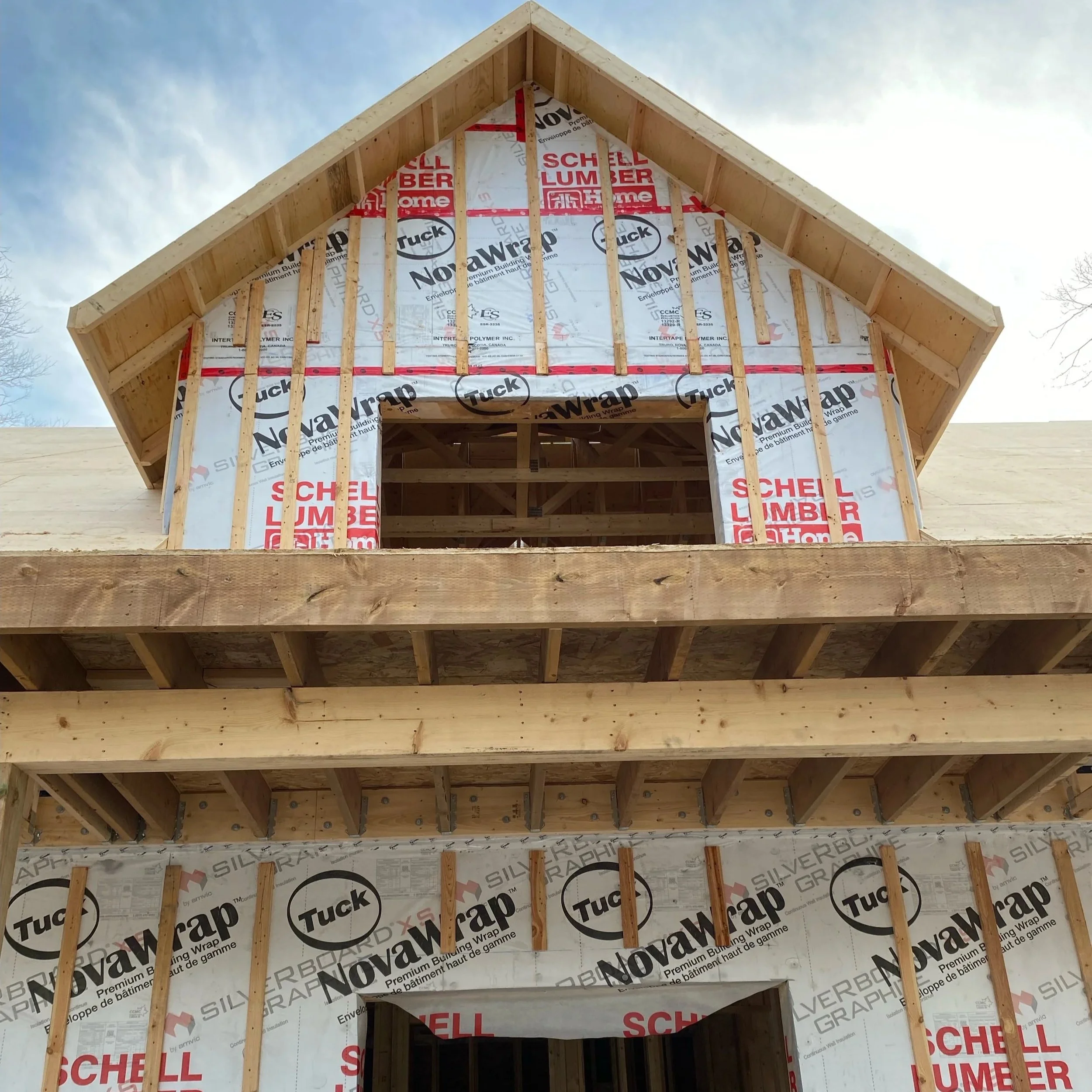 A partially constructed house with an exposed roof and walls covered in building wrap. The roof has wooden framing with plywood sheathing visible underneath.