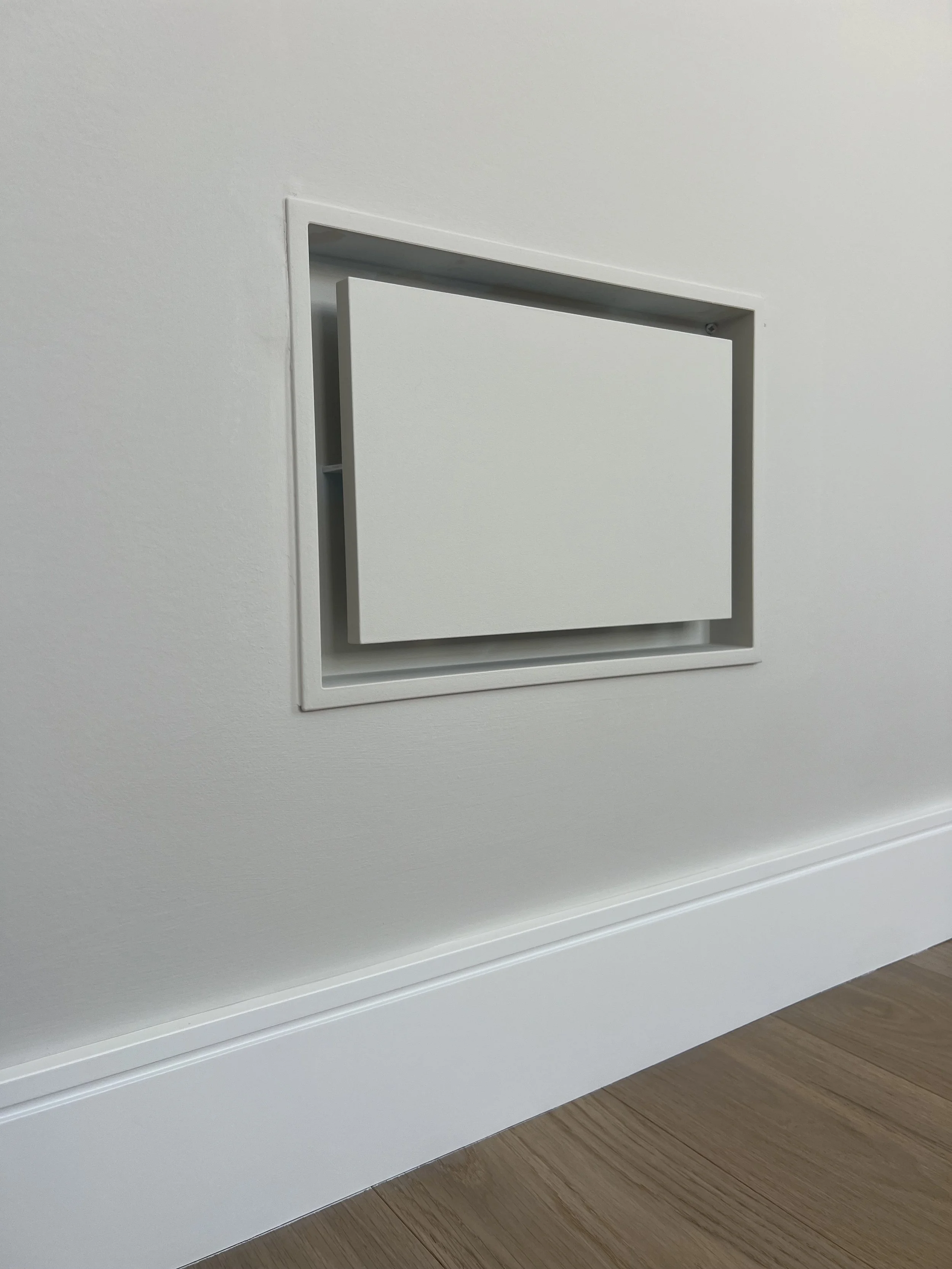 Close-up of a white wall vent near the baseboard on light wood flooring.