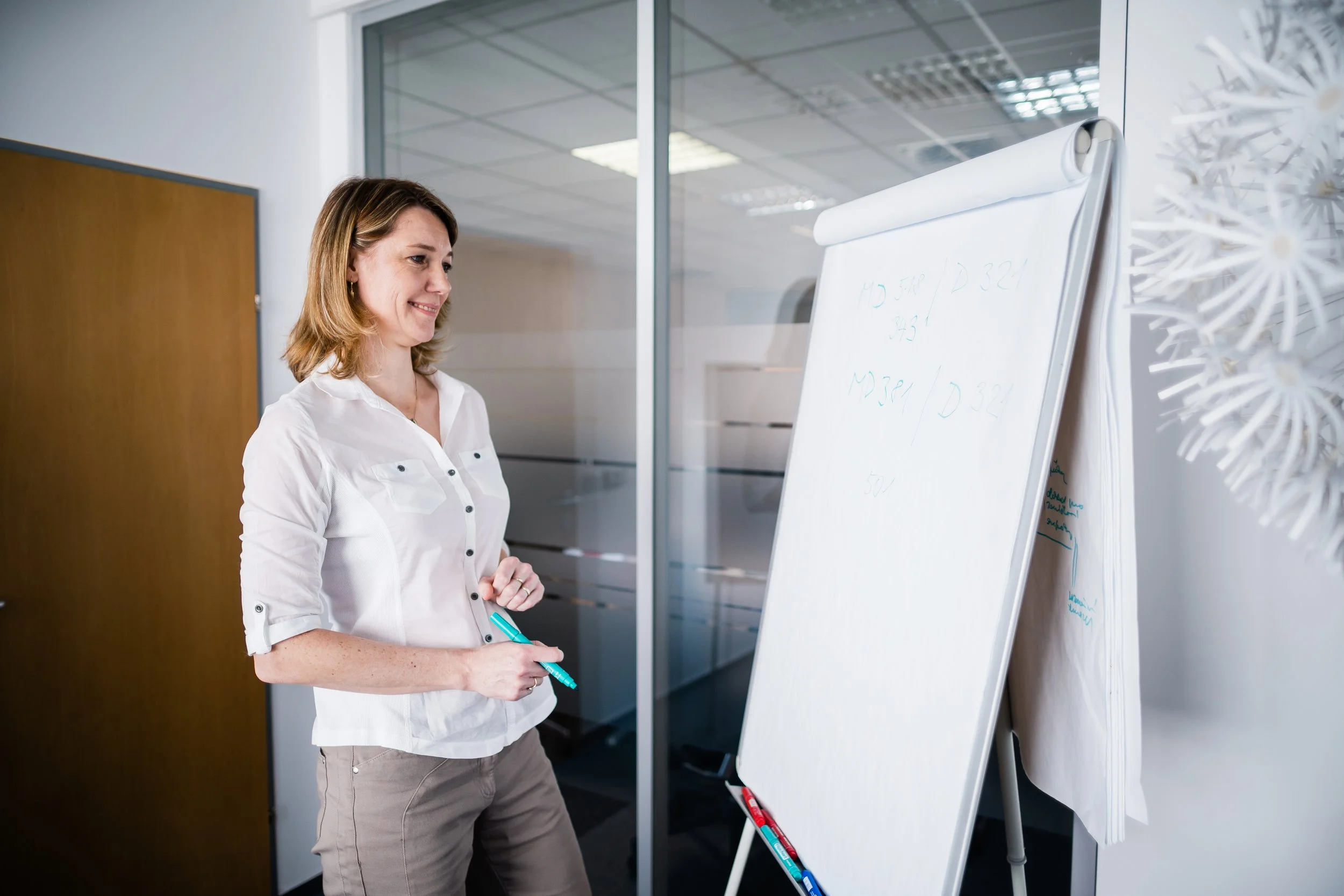 A woman standing in an office looking at a whiteboard with faint writing, holding a blue marker. Modern light corporate company employer branding photography in Zürich, Zug, Bern, Lucerne, Basel, St. Gallen and across Switzerland.