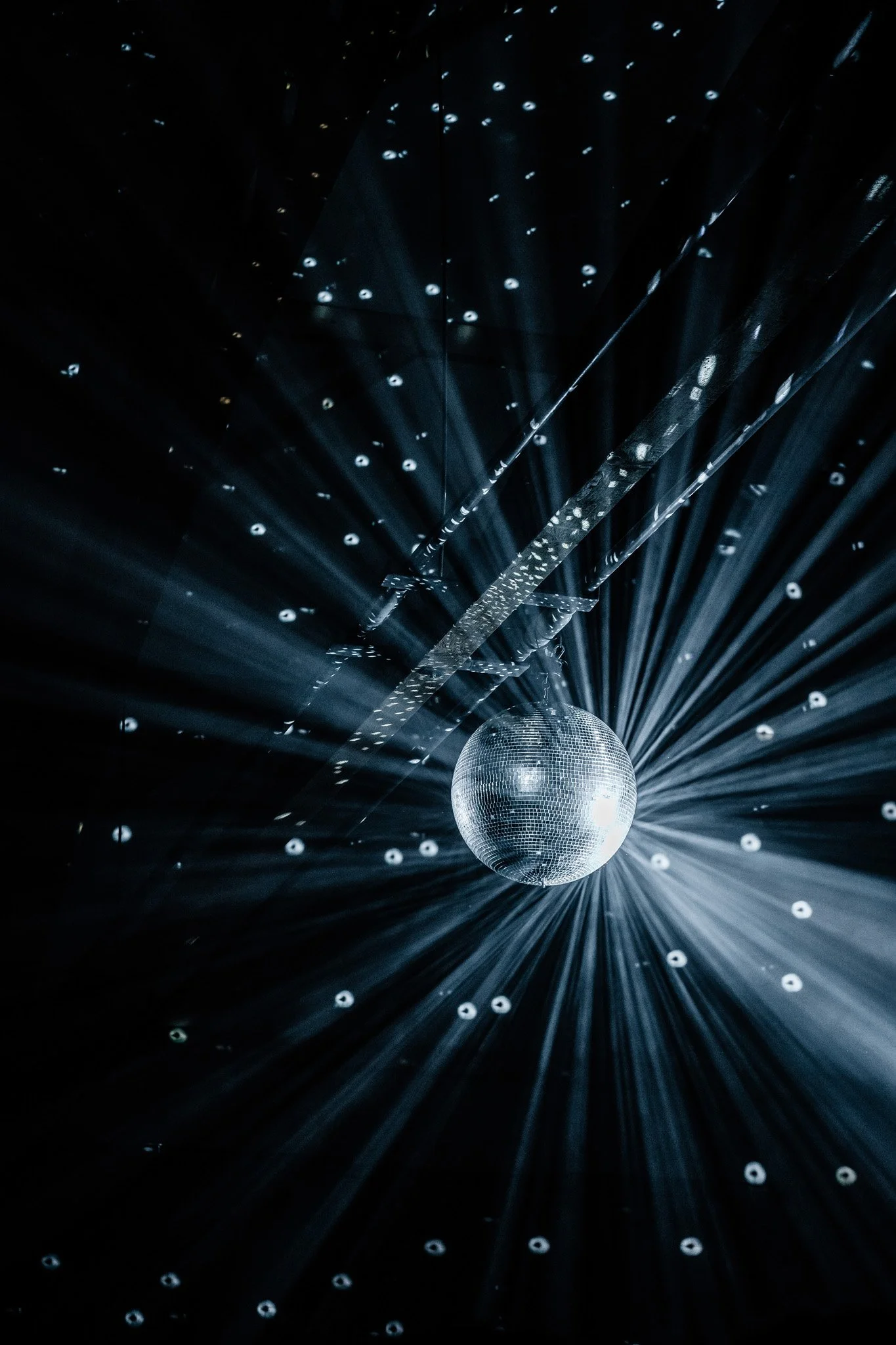 A disco ball reflecting light, creating beams and small reflections on a dark background. Concert photographer in Switzerland.