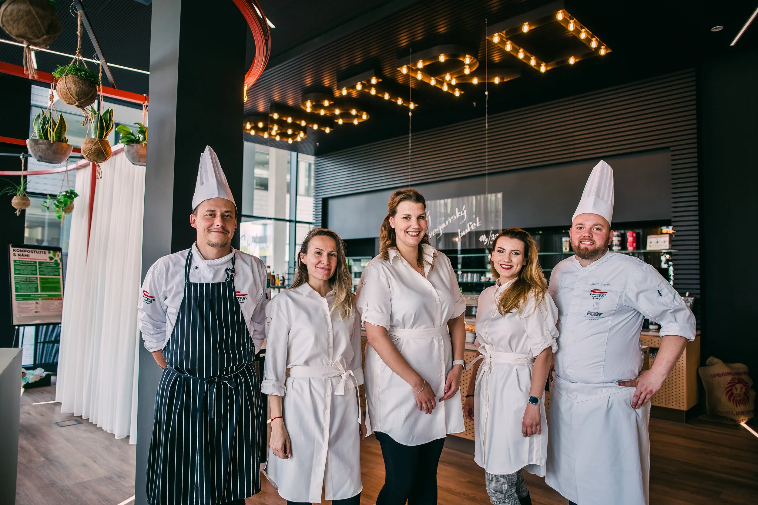 Group of five chefs and restaurant staff standing together inside a modern, stylish restaurant kitchen or dining area, smiling at the camera, with decor and lighting overhead. Restuarant interior photography and chef, waiters team in Switzerland.