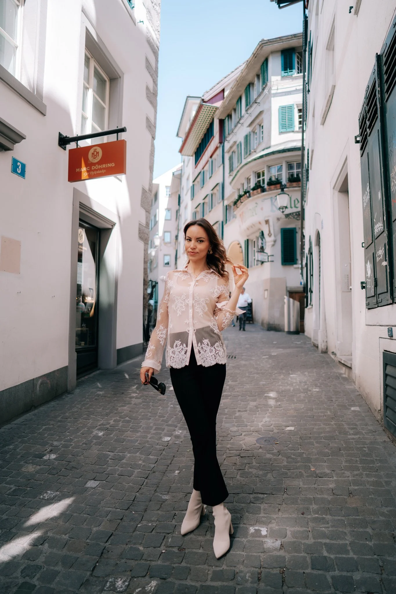 Young woman in a lace blouse and black pants walking on a cobblestone street in Zurich, Switzerland.