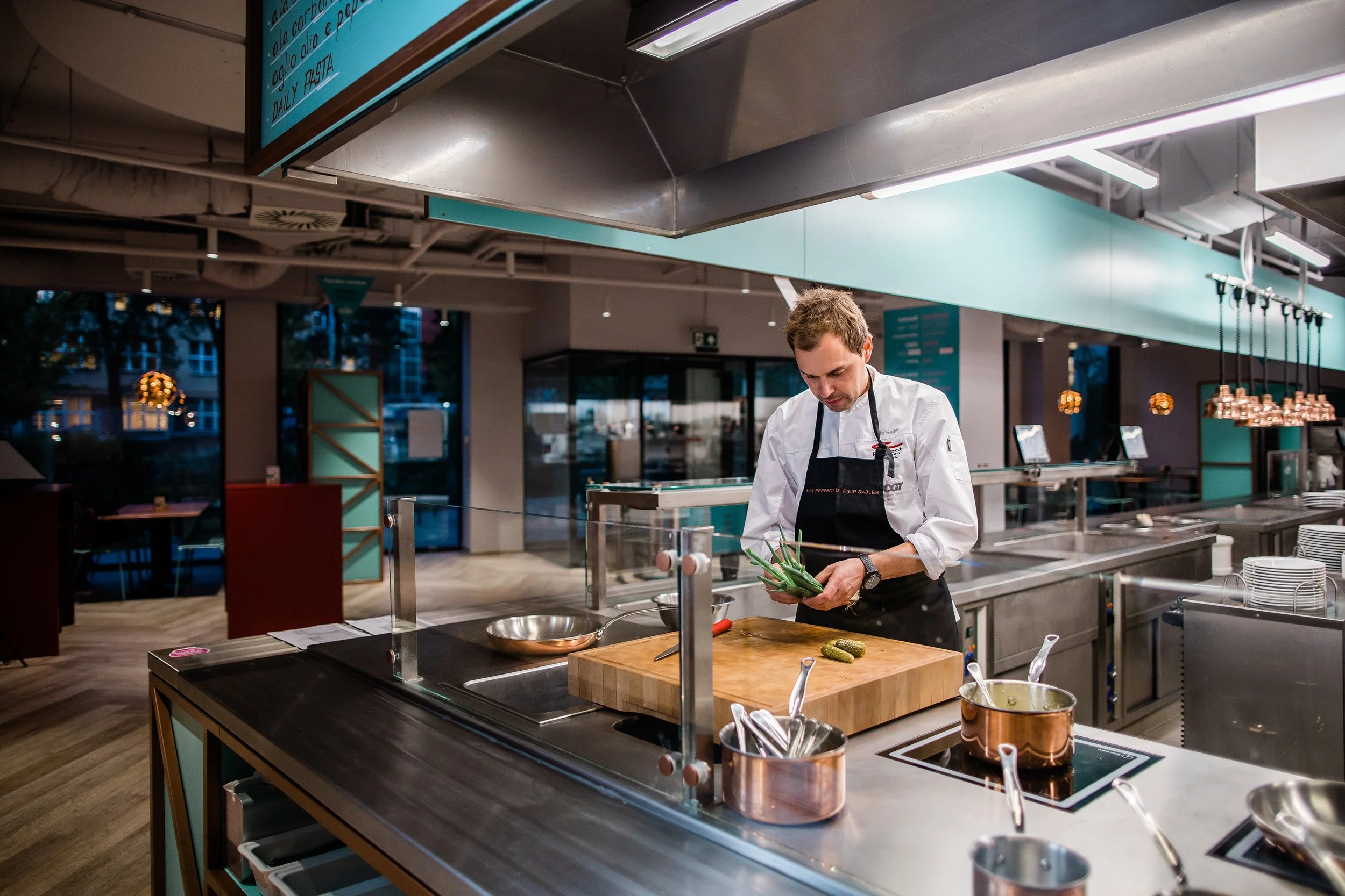 A chef in a white uniform and black apron preparing green onions in a professional kitchen. Personal branding and fine dining restaurant photography in Zürich, Zug, Bern, Lucerne, Basel, St. Gallen and across Switzerland.