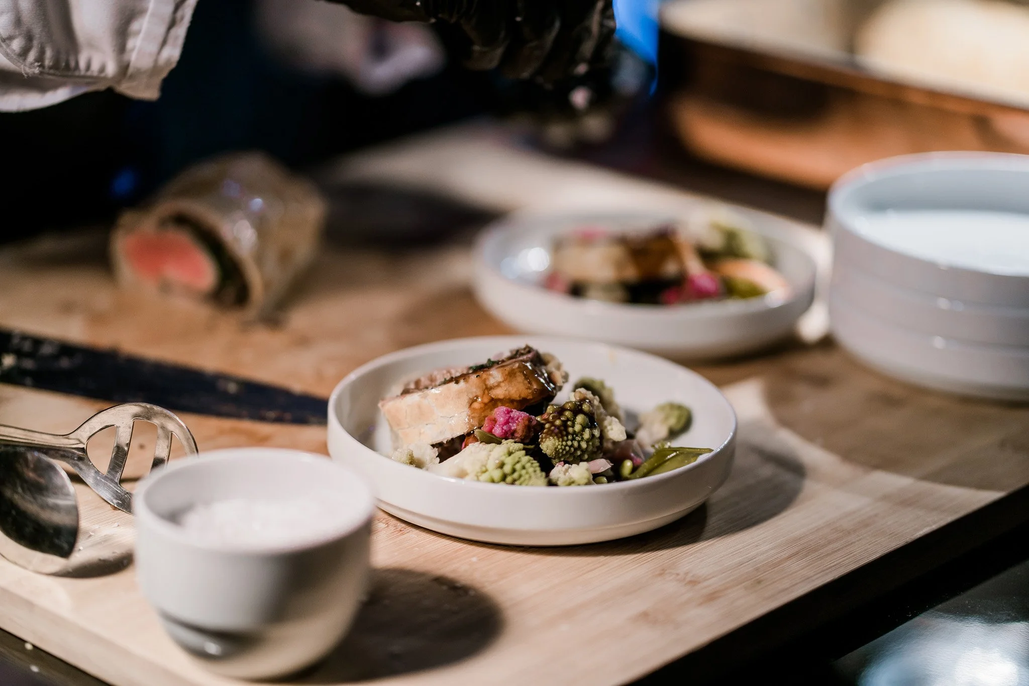A kitchen scene with sliced sushi rolls, fresh vegetables, and a bowl of water on a wooden cutting board. Catering, culinary and food photography in Zürich, Zug, Bern, Lucerne, Basel, St. Gallen and across Switzerland.