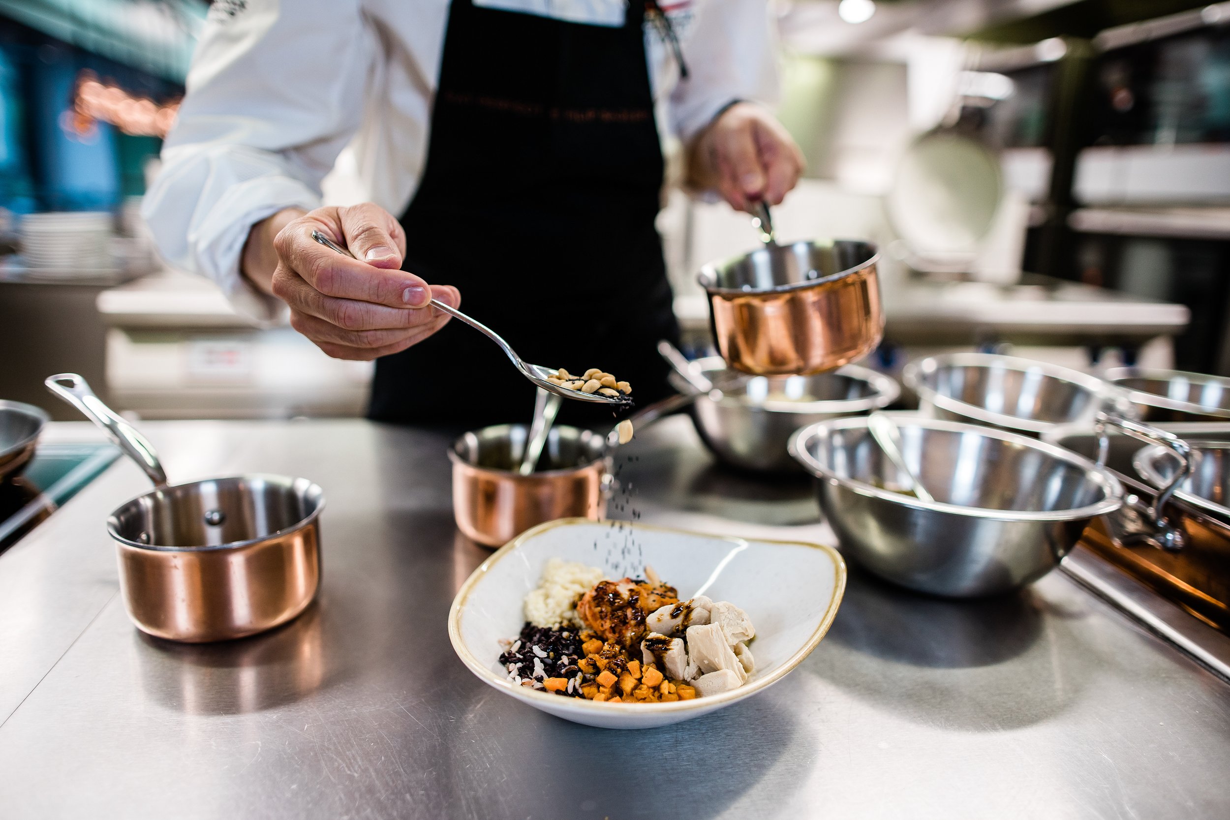 A chef is adding seasoning to a plated dish in a professional kitchen with stainless steel cookware and utensils. Personal branding and fine dining restaurant photography in Zürich, Zug, Bern, Lucerne, Basel, St. Gallen and across Switzerland.