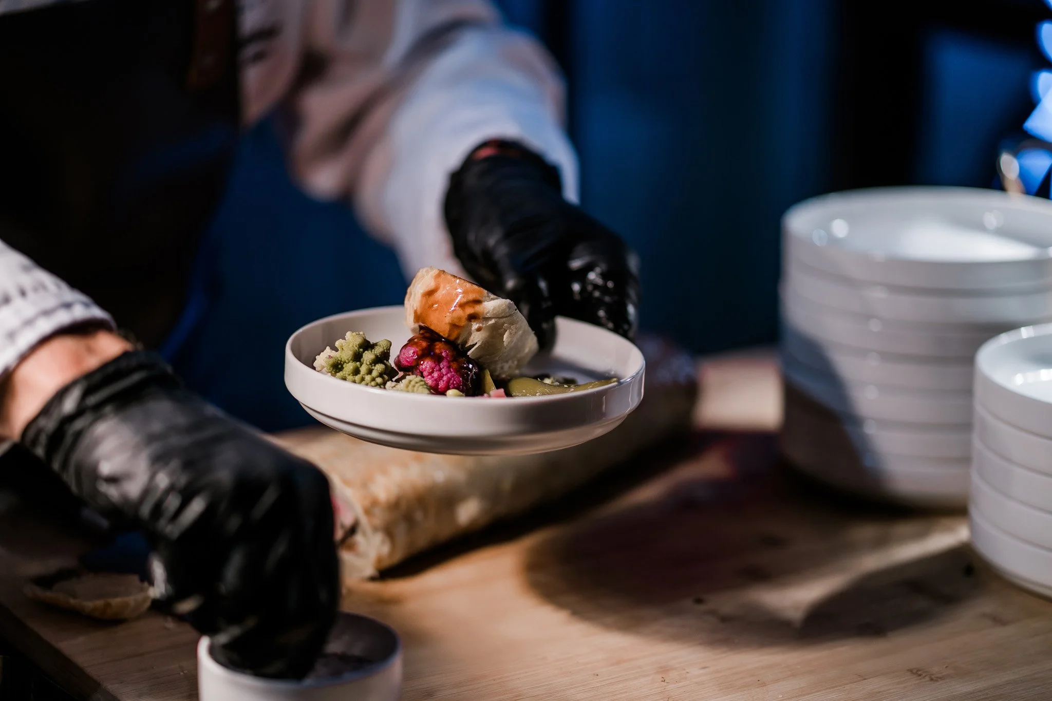Person with black gloves serving a bowl of ice cream topped with fruit and cookies at a restaurant or cafe setting. Catering and food photography in Zürich, Zug, Bern, Lucerne, Basel, St. Gallen and across Switzerland.