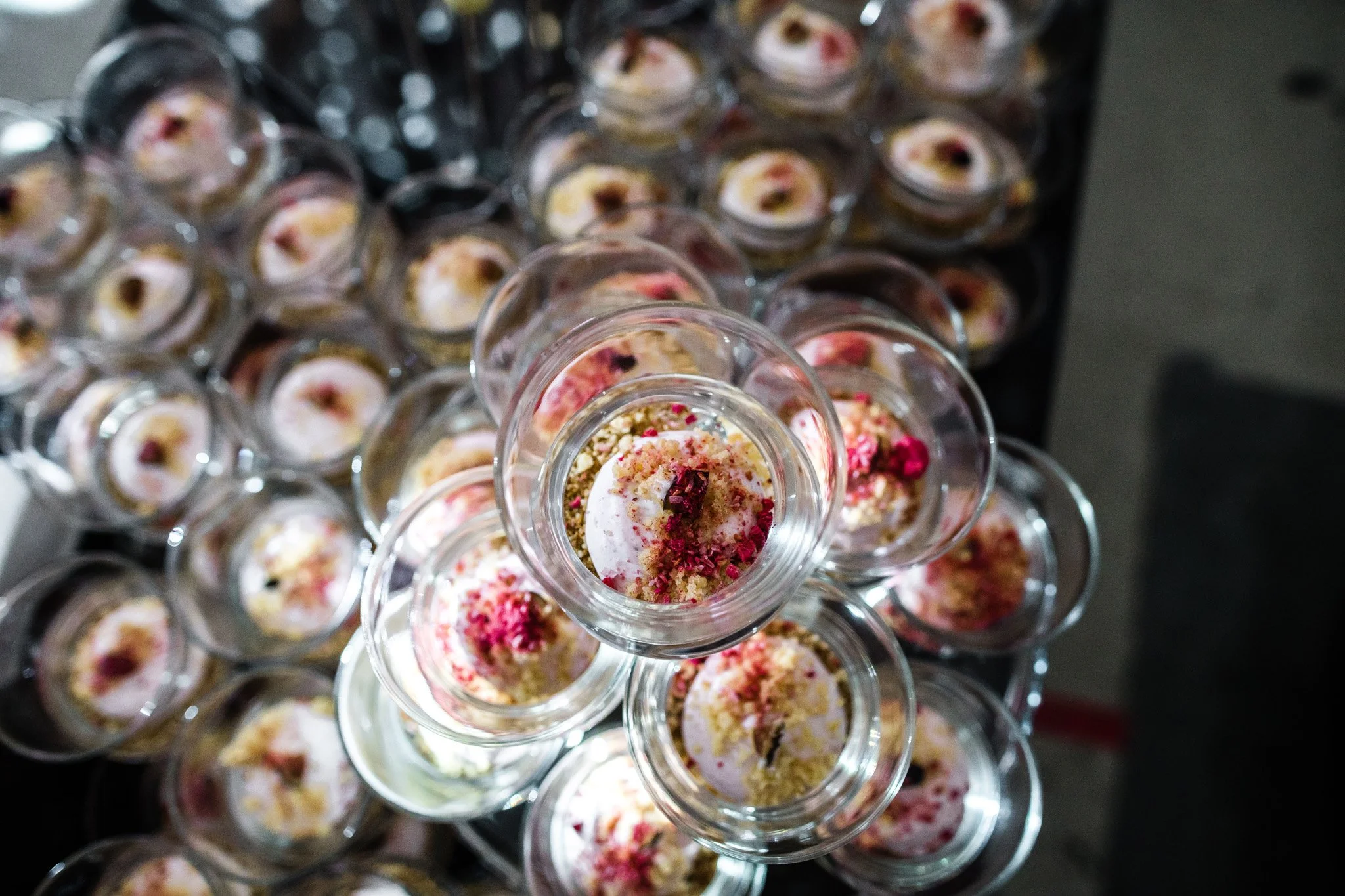Multiple glass cups with dessert topped with pink and white flower petals, viewed from above. Catering, culinary and food photography in Zürich, Zug, Bern, Lucerne, Basel, St. Gallen and across Switzerland.
