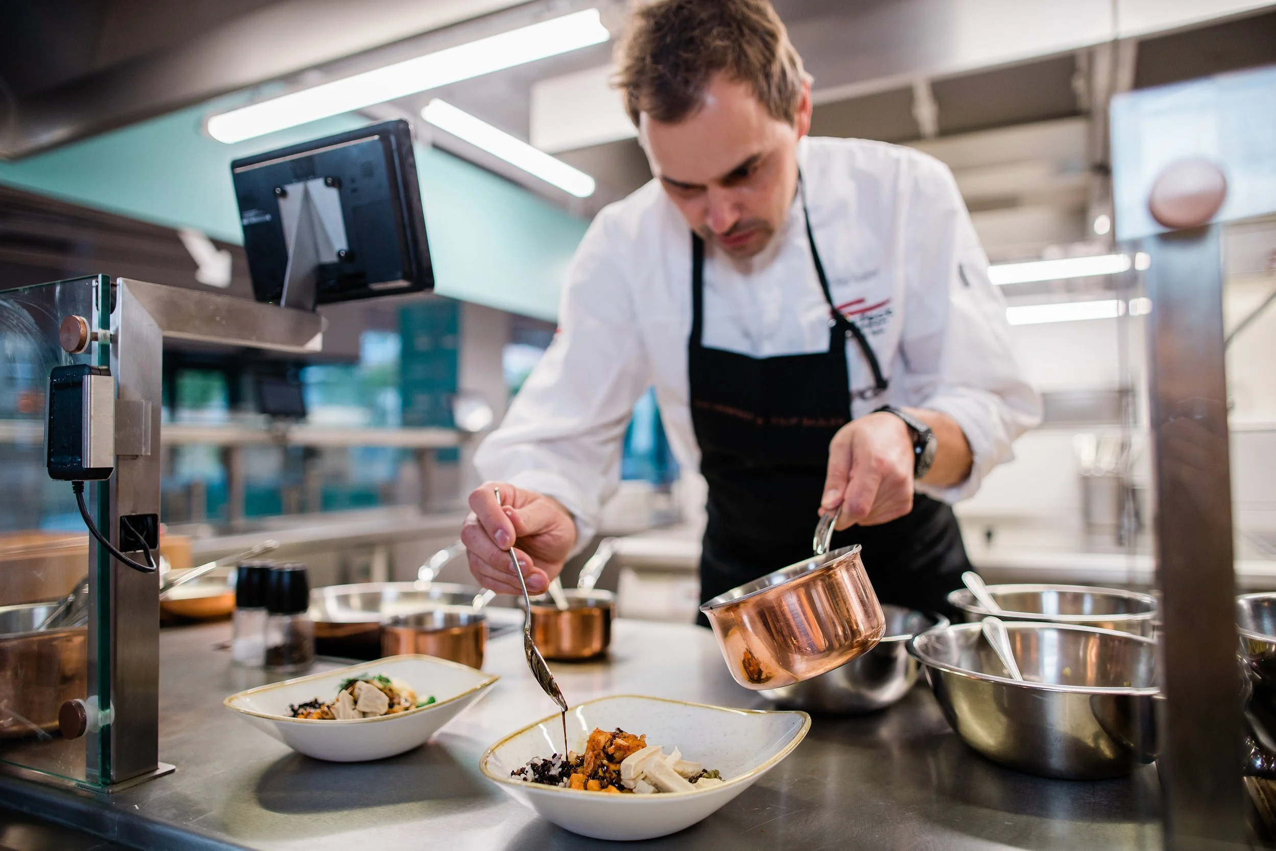 Chef plating a dish in a professional kitchen, with various bowls and utensils on the counter. Personal branding and fine dining restaurant photography in Zürich, Zug, Bern, Lucerne, Basel, St. Gallen and across Switzerland.