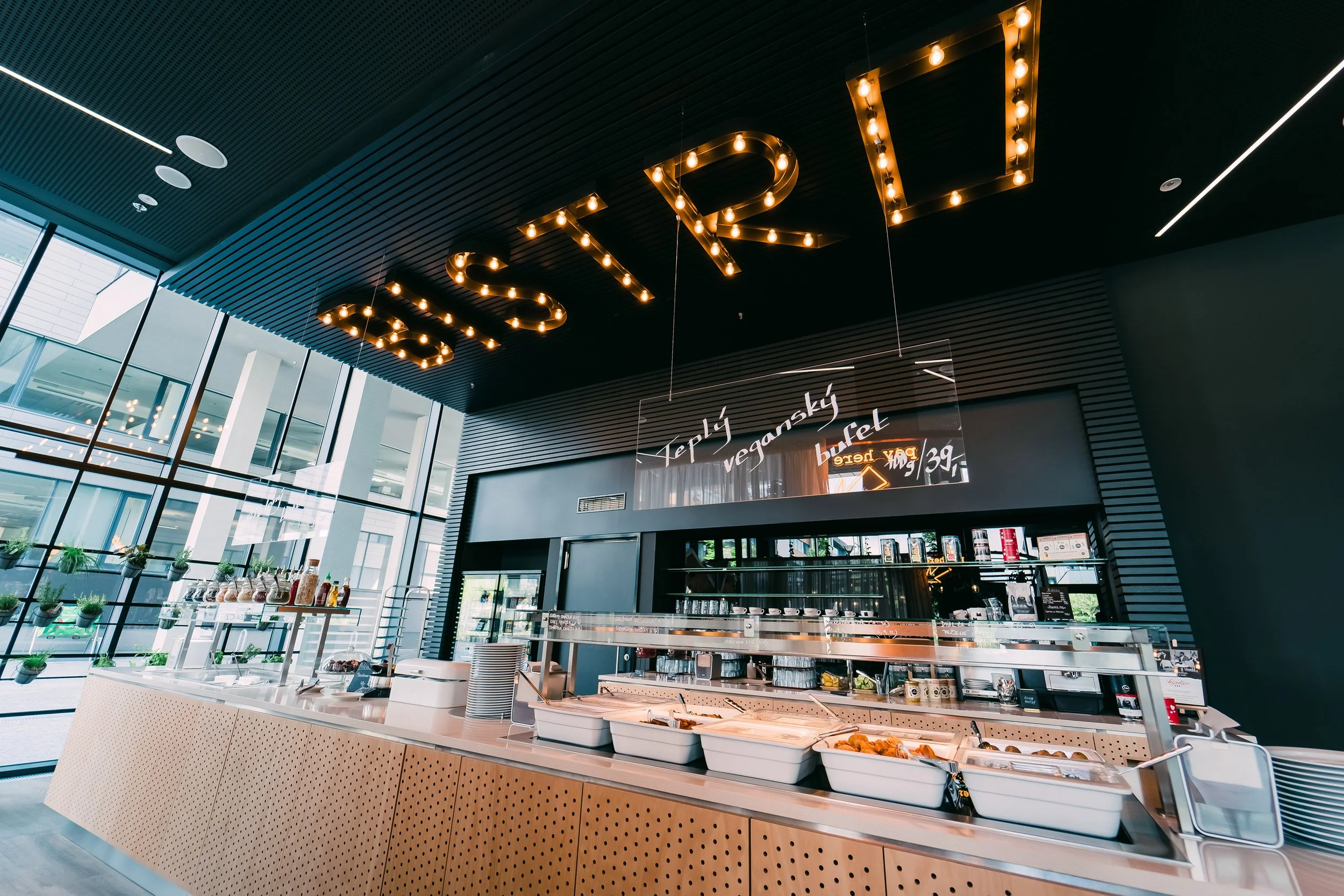 Modern restaurant or cafe interior with a buffet counter, black and wood decor, large windows, and illuminated sign spelling fleur. Restaurant interior photography in Zürich, Zug, Bern, Lucerne, Basel, St. Gallen and across Switzerland.