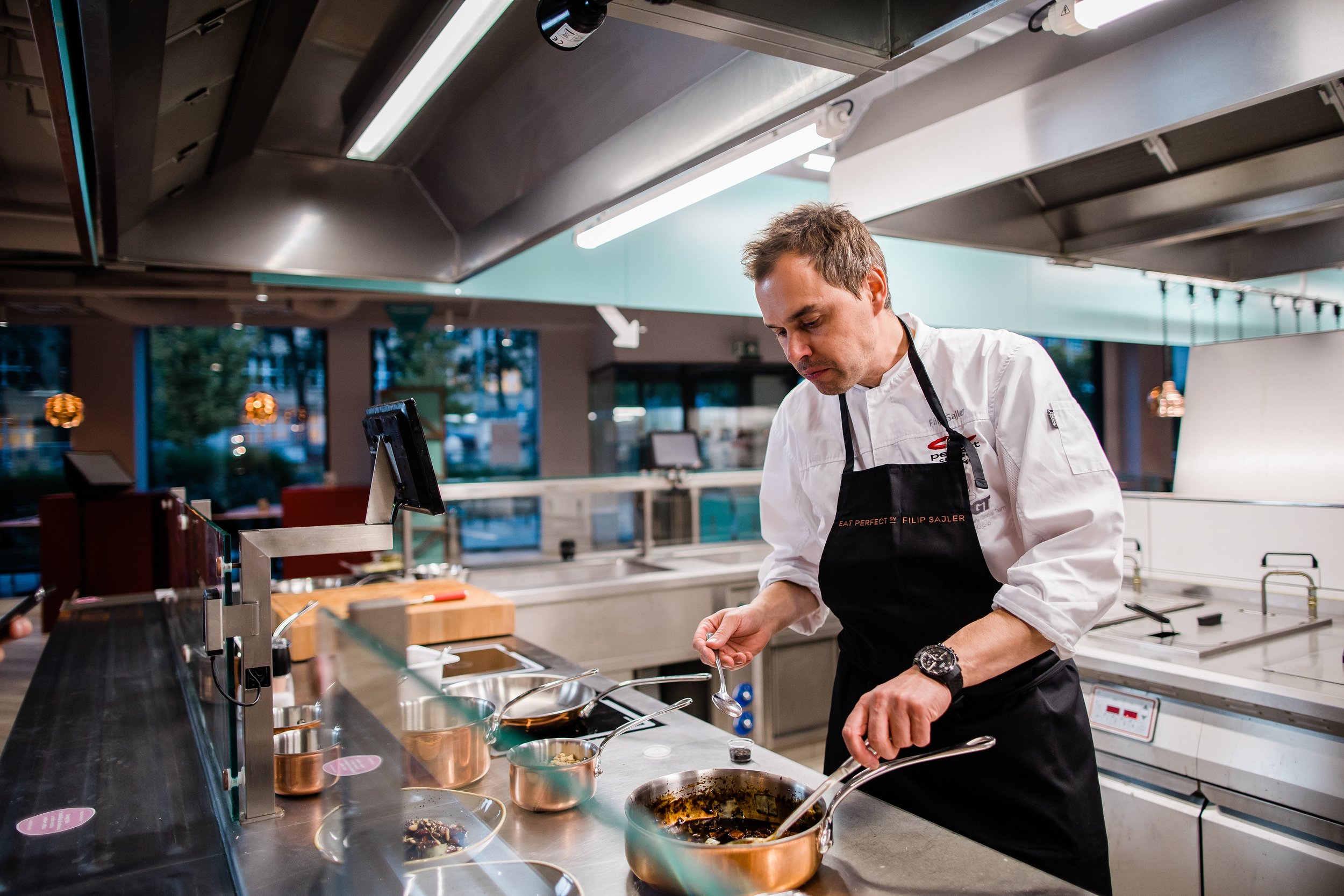 Chef cooking in a modern kitchen, stirring a pan on the stove with various utensils and ingredients around. Personal branding and fine dining restaurant photography in Zürich, Zug, Bern, Lucerne, Basel, St. Gallen and across Switzerland.