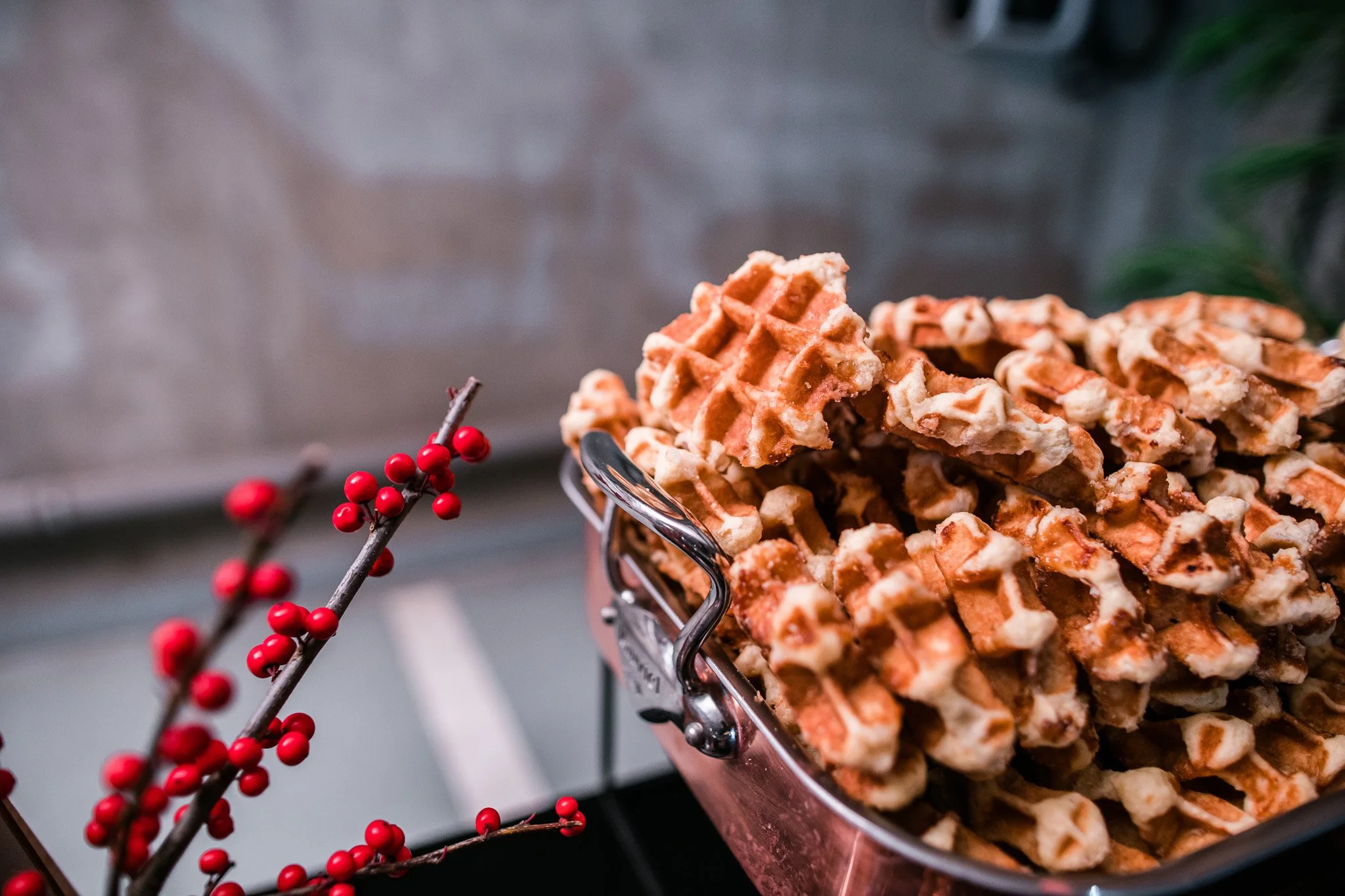 A large basket of waffles with syrup and a decorative branch with red berries in the foreground. Catering and food photography in Zürich, Zug, Bern, Lucerne, Basel, St. Gallen and across Switzerland.