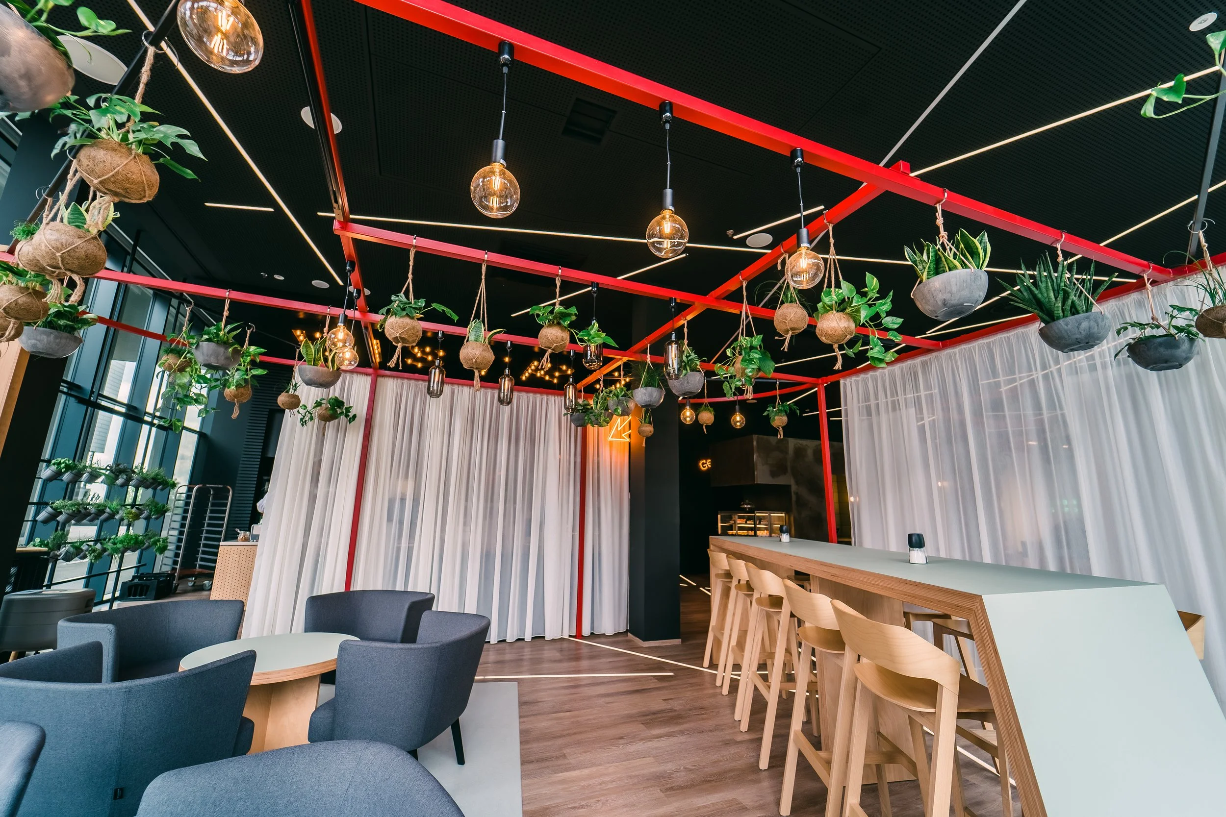 Modern restaurant interior with hanging potted plants, pendant lights, a white curtain dividing area, and table seating including bar and lounge chairs. Restaurant interior photography in Zürich, Zug, Bern, Lucerne, Basel, St. Gallen and Switzerland.