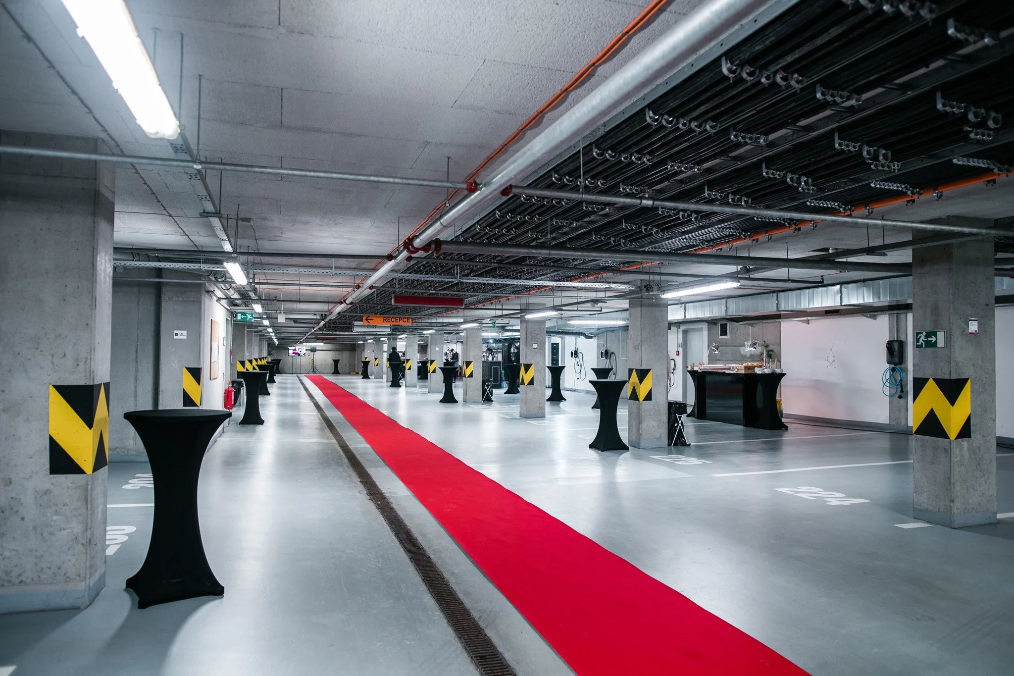 Underground parking garage with a red carpet walkway, high ceilings with visible pipes and cables, and black high-top tables set up for an event. Event photography Switzerland.