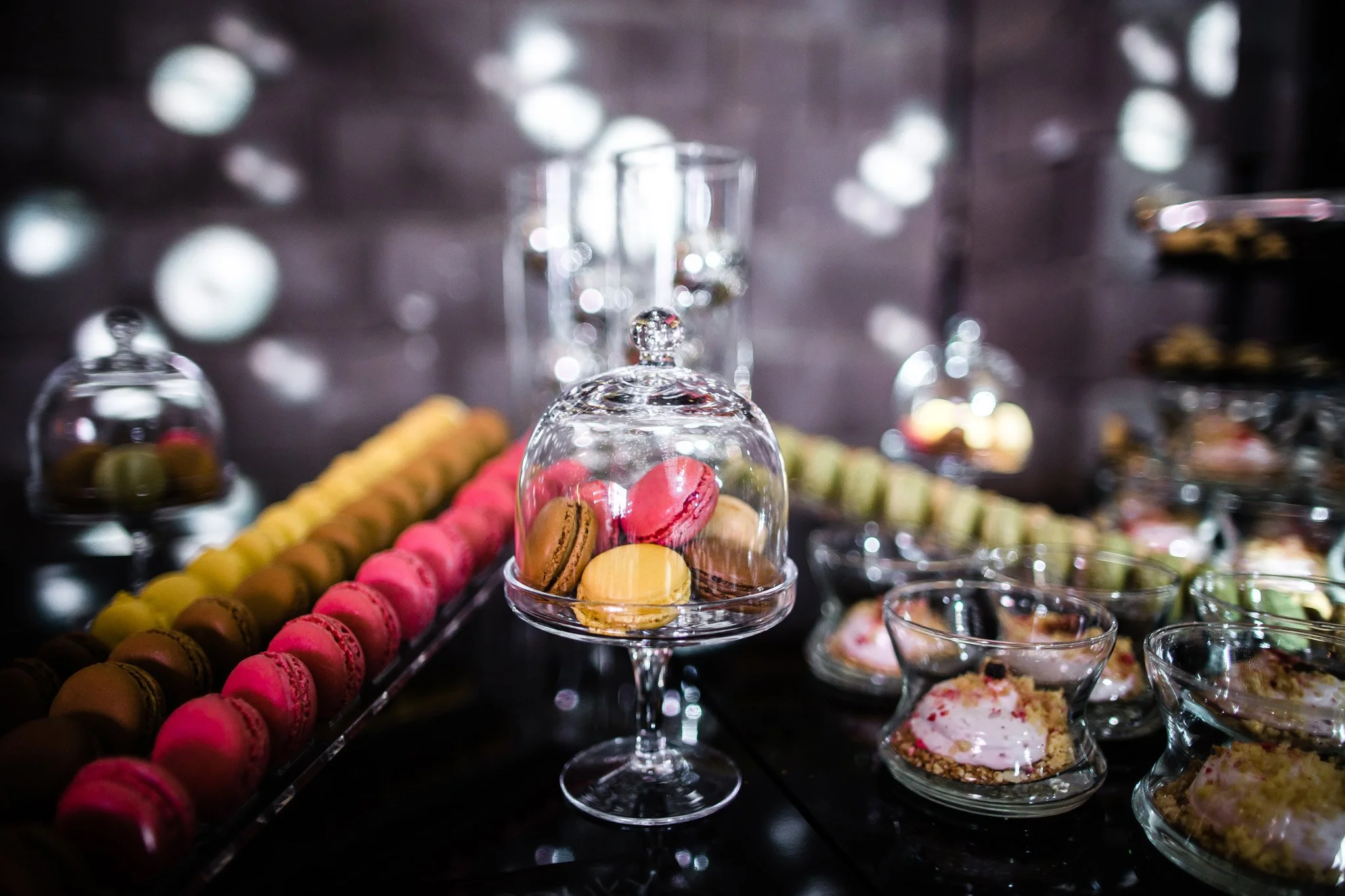 Assorted colorful macarons displayed under glass cloches and in bowls on a dessert table. Catering, culinary and food photography in Zürich, Zug, Bern, Lucerne, Basel, St. Gallen and across Switzerland.