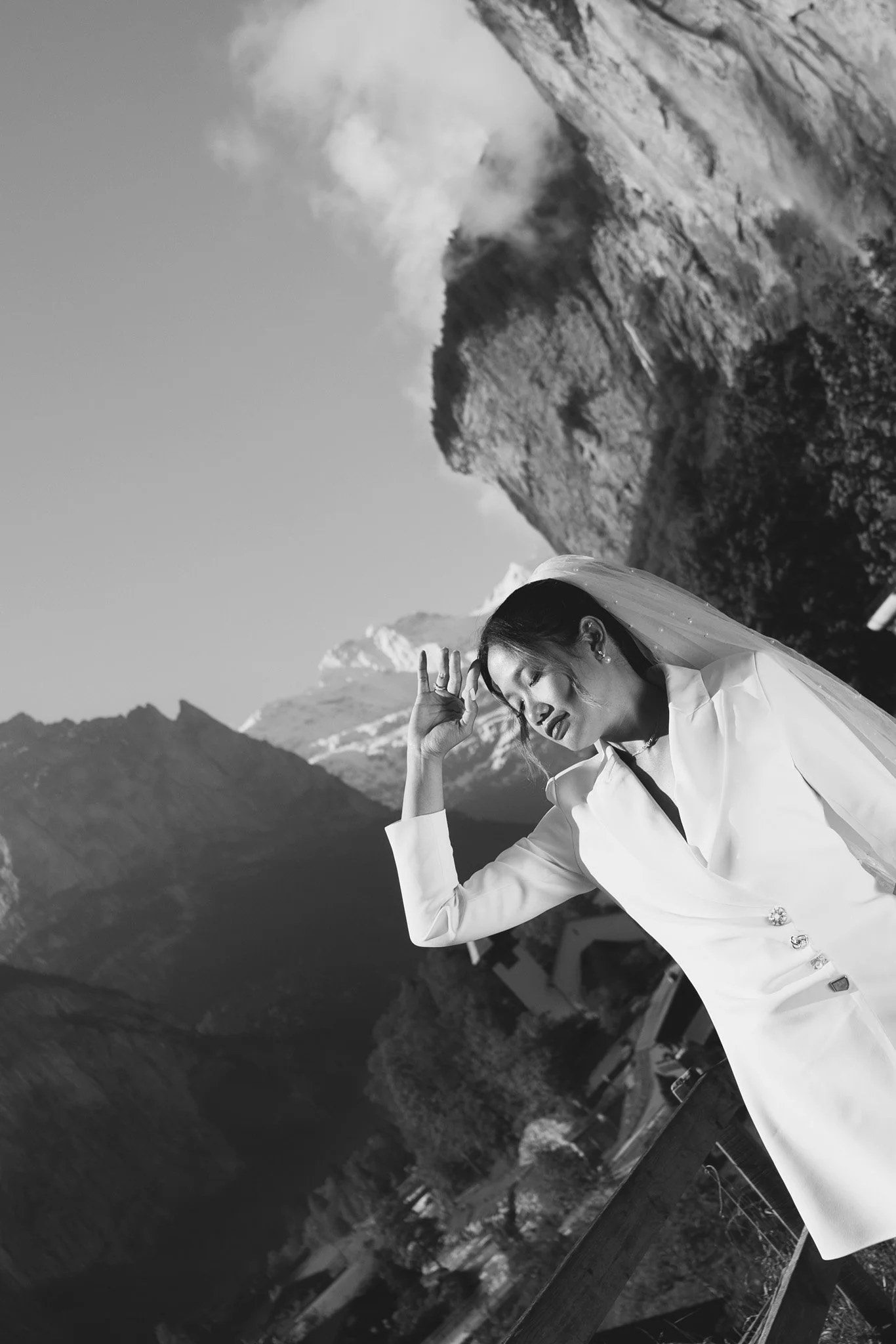 A woman wearing a wedding dress and veil, standing outdoors near a wooden railing, with mountains of Lauterbrunnen Valley in Swiss Alps.