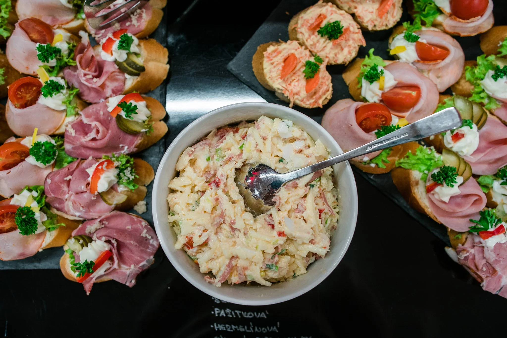 Various open-faced sandwiches with meats, vegetables, and condiments surrounding a bowl of potato salad. Catering and food photography in Zürich, Zug, Bern, Lucerne, Basel, St. Gallen and across Switzerland.