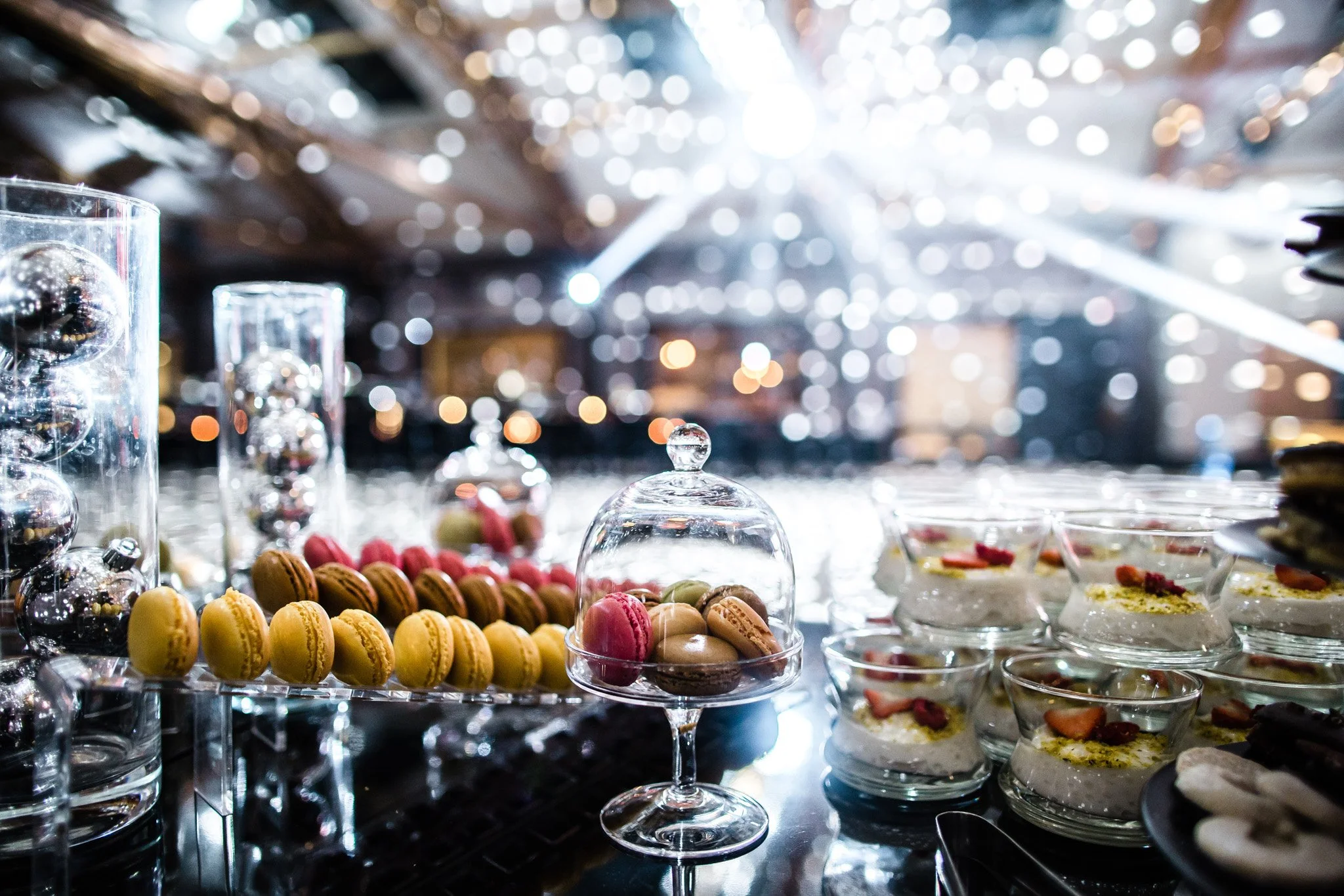 A dessert table with colorful macarons, chocolates, and other sweets under bright, festive lighting. Catering, culinary and food photography in Zürich, Zug, Bern, Lucerne, Basel, St. Gallen and across Switzerland.