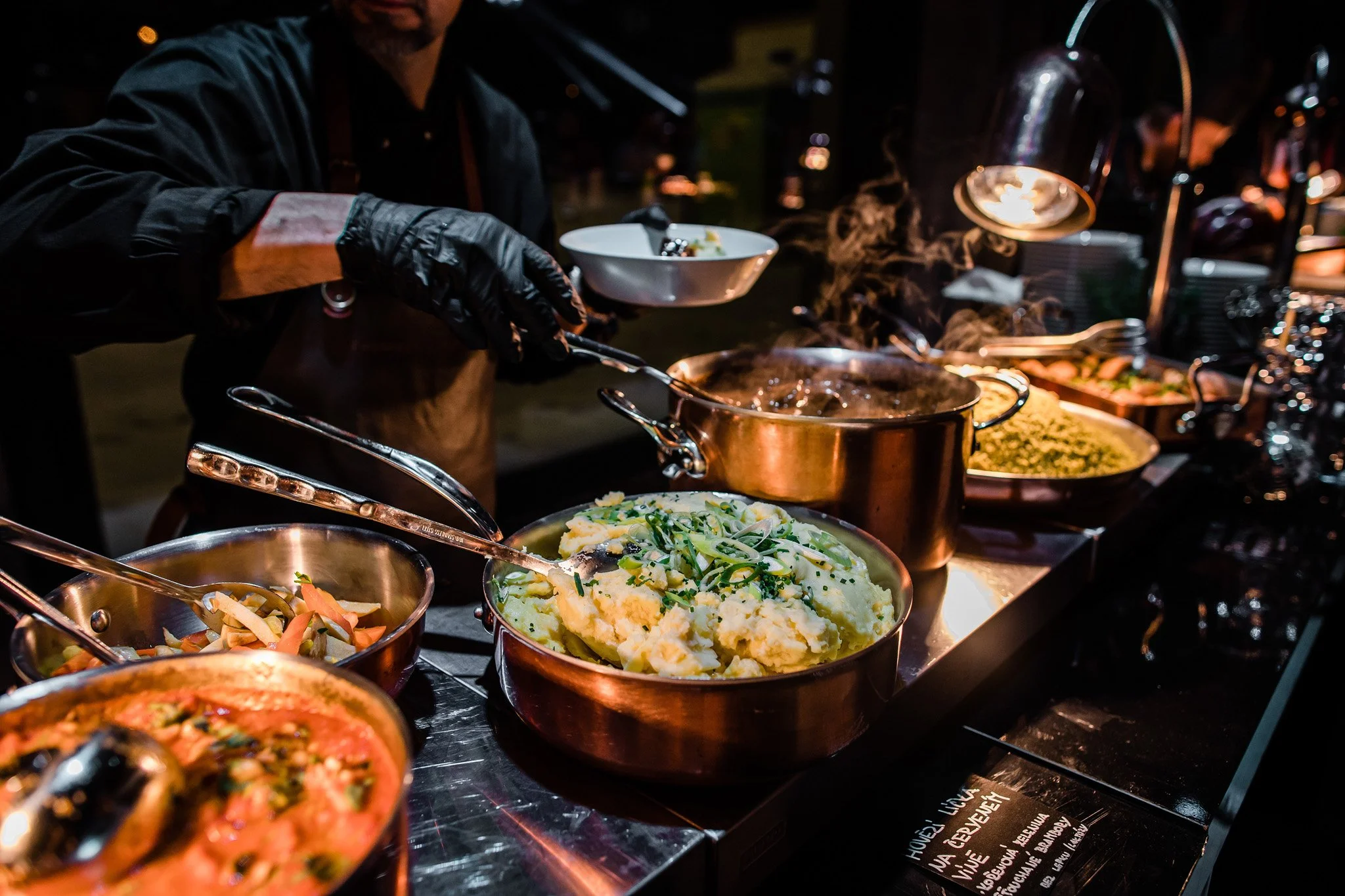 Buffet of hot dishes including mashed potatoes, vegetables, and stews in a buffet setting with warm lighting. Catering, culinary and food photography in Zürich, Zug, Bern, Lucerne, Basel, St. Gallen and across Switzerland.