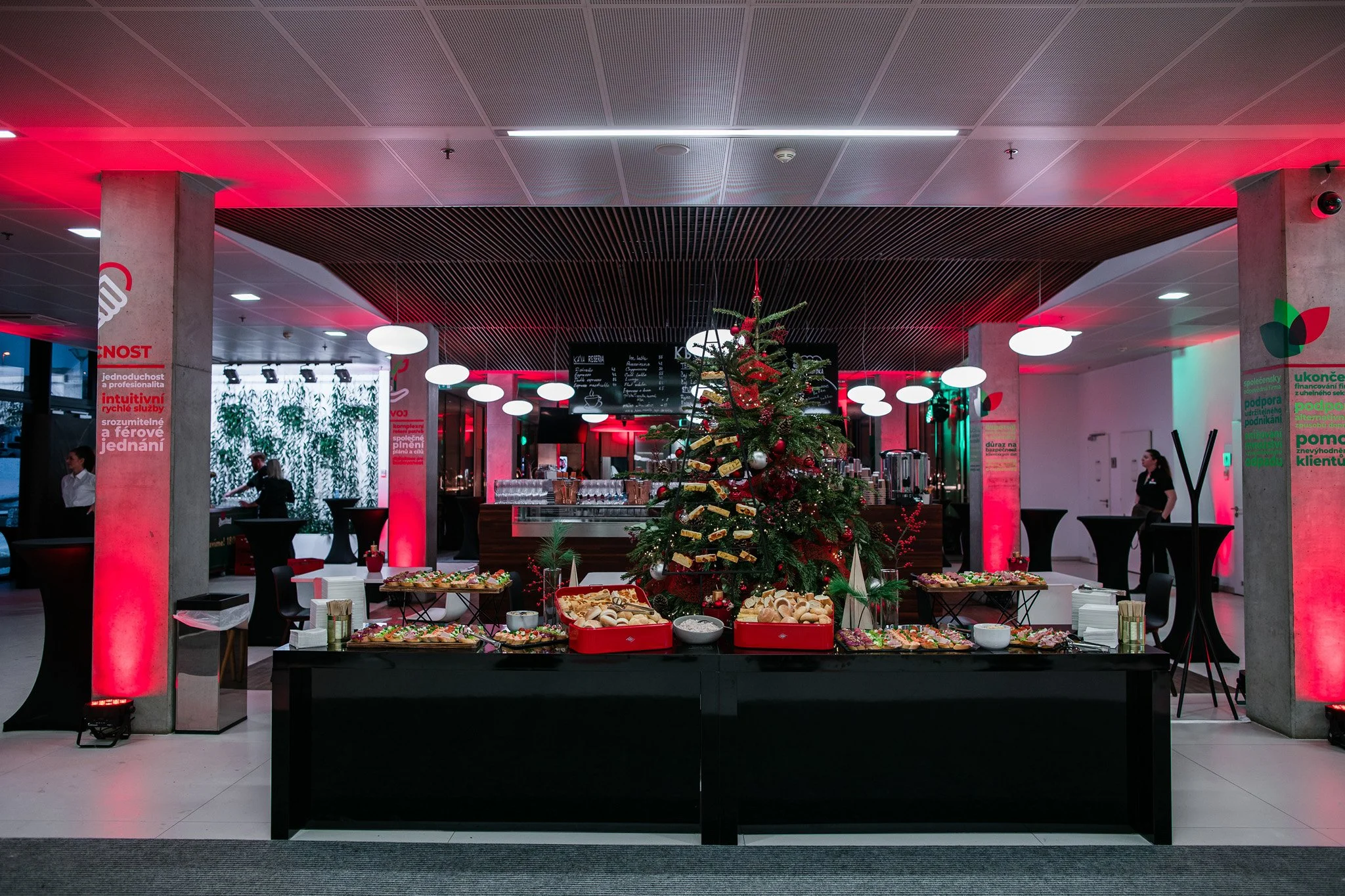 A decorated Christmas tree surrounded by snacks and treats at a holiday event in a modern indoor setting with red and green lighting. Catering, culinary and food photography in Zürich, Zug, Bern, Lucerne, Basel, St. Gallen and across Switzerland.