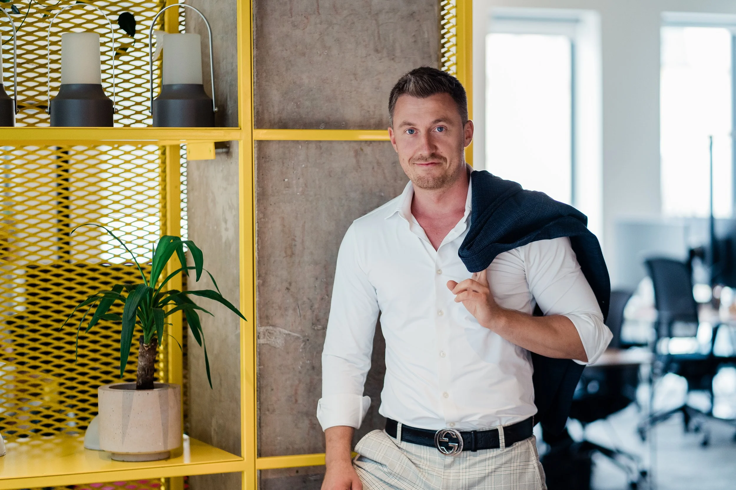 A man in a white shirt and plaid pants standing indoors in the office. Professional modern business headshot portrait photography in Zürich, Zug, Bern, Lucerne, Basel, St. Gallen and across Switzerland. Personal branding in corporate or startup.