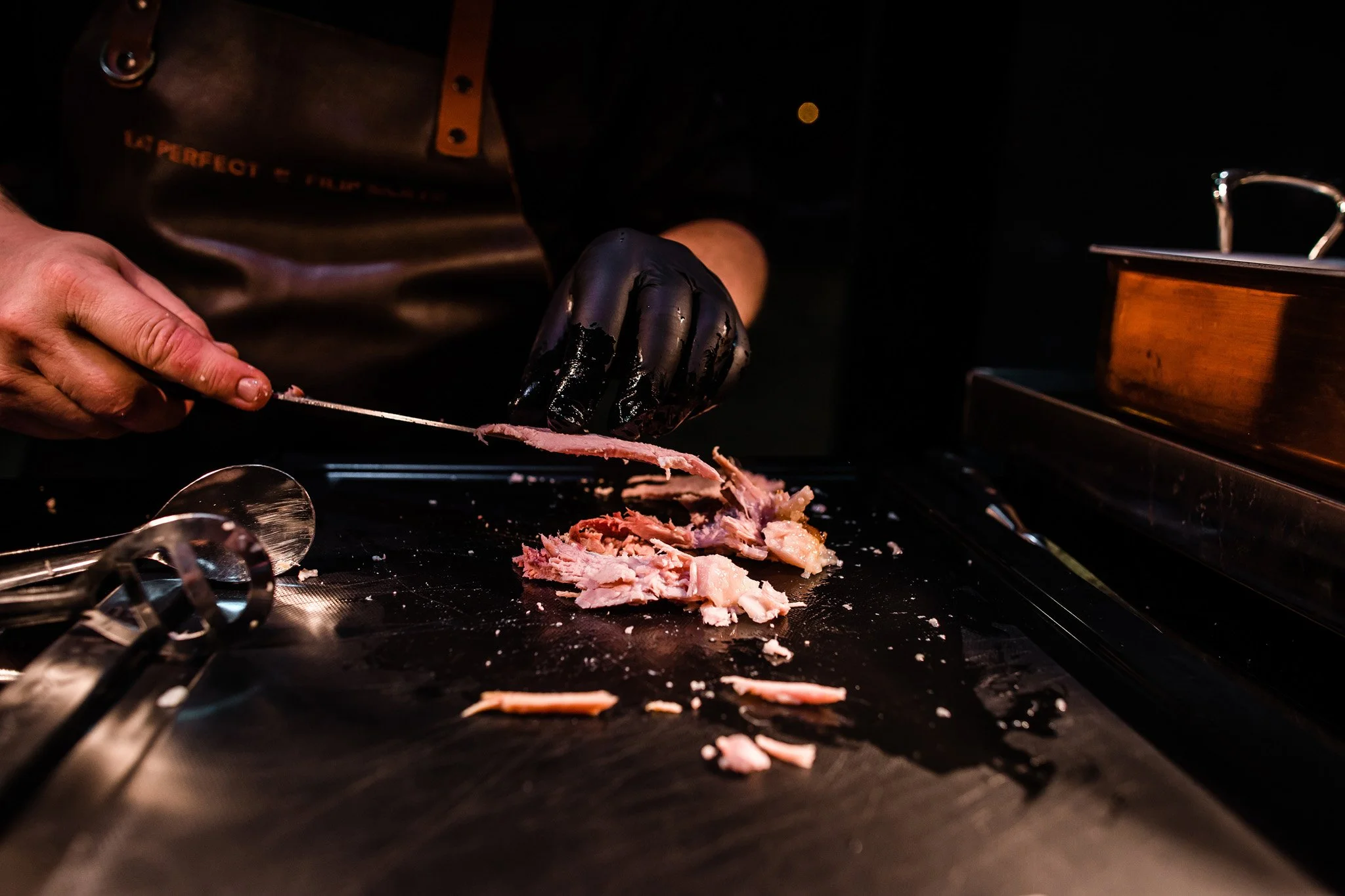 Person slicing cooked meat on a black countertop with kitchen utensils nearby. Catering, culinary and food photography in Zürich, Zug, Bern, Lucerne, Basel, St. Gallen and across Switzerland.