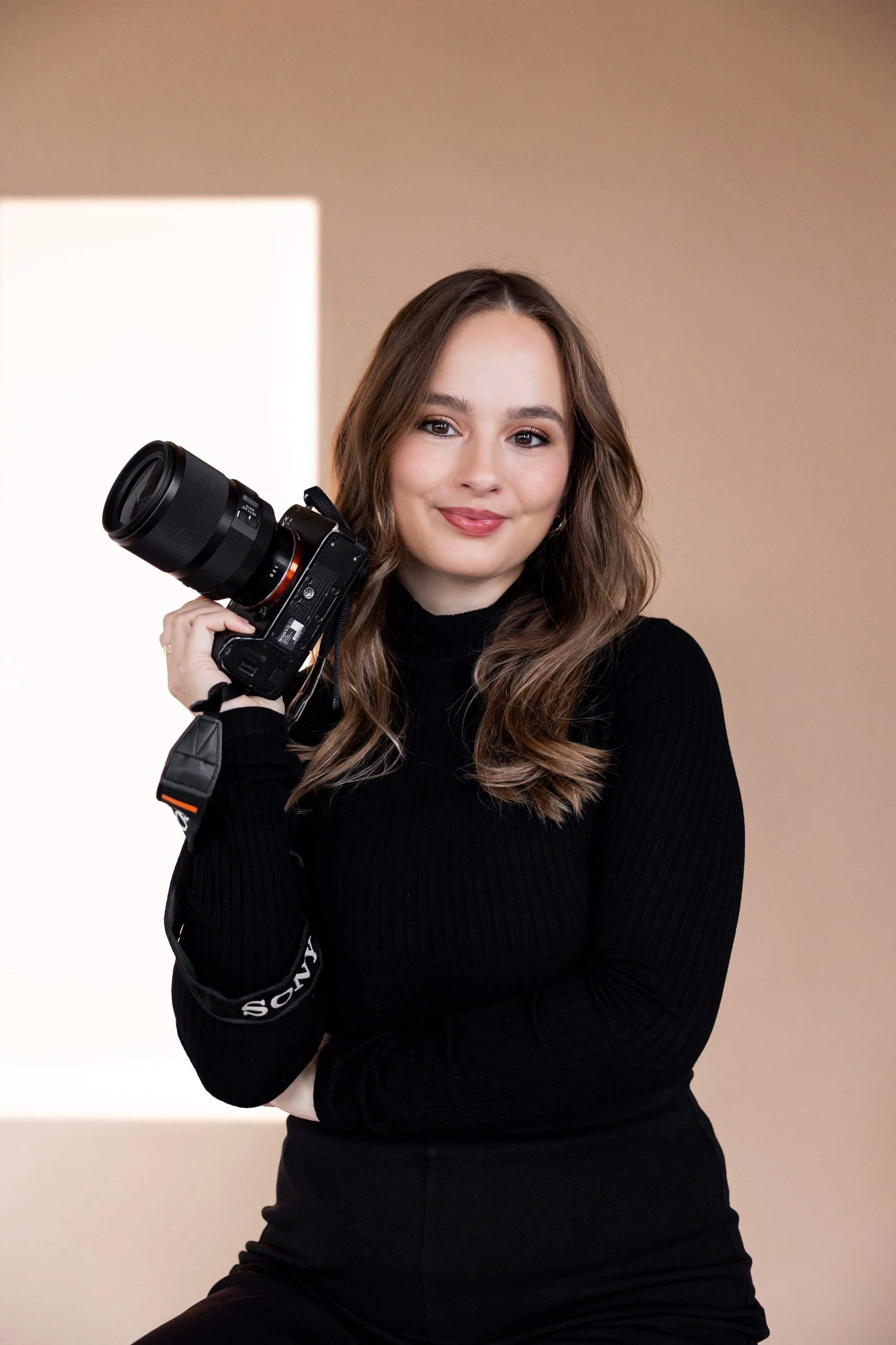 Switzerland vacation photographer with wavy brown hair holding a professional camera, smiling, against a neutral background.
