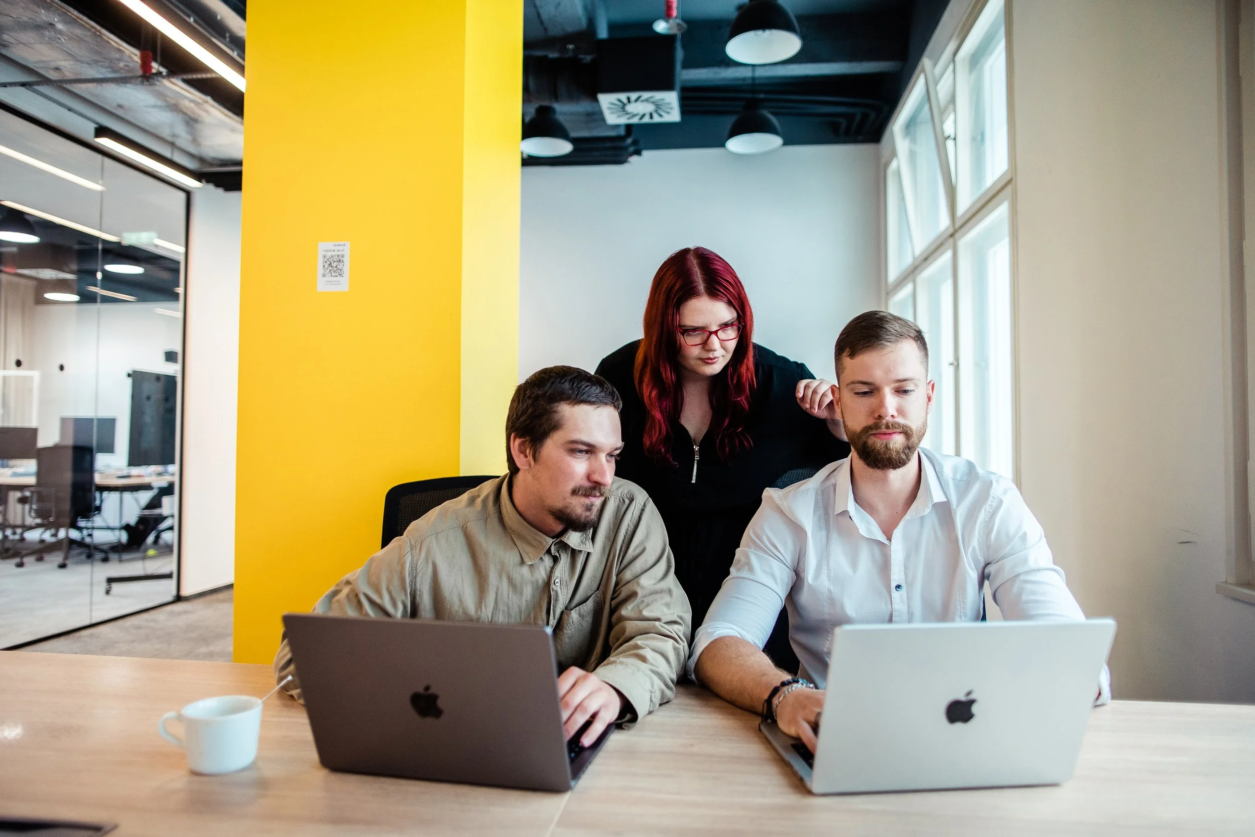 Three people working together on laptops in a modern office with large windows and a yellow accent wall. Modern office employer branding photography in Zürich, Zug, Bern, Lucerne, Basel, St. Gallen and across Switzerland.