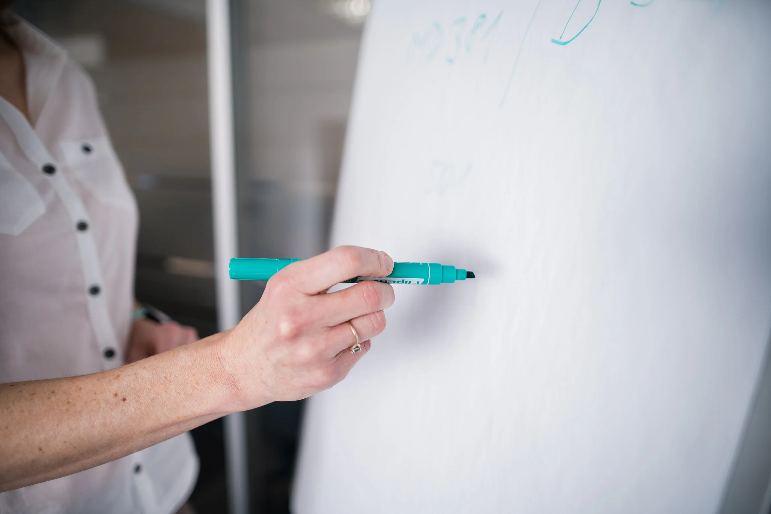 Person writing on a whiteboard with a blue marker, wearing a light-colored shirt. Modern light corporate company employer branding photography in Zürich, Zug, Bern, Lucerne, Basel, St. Gallen and across Switzerland.