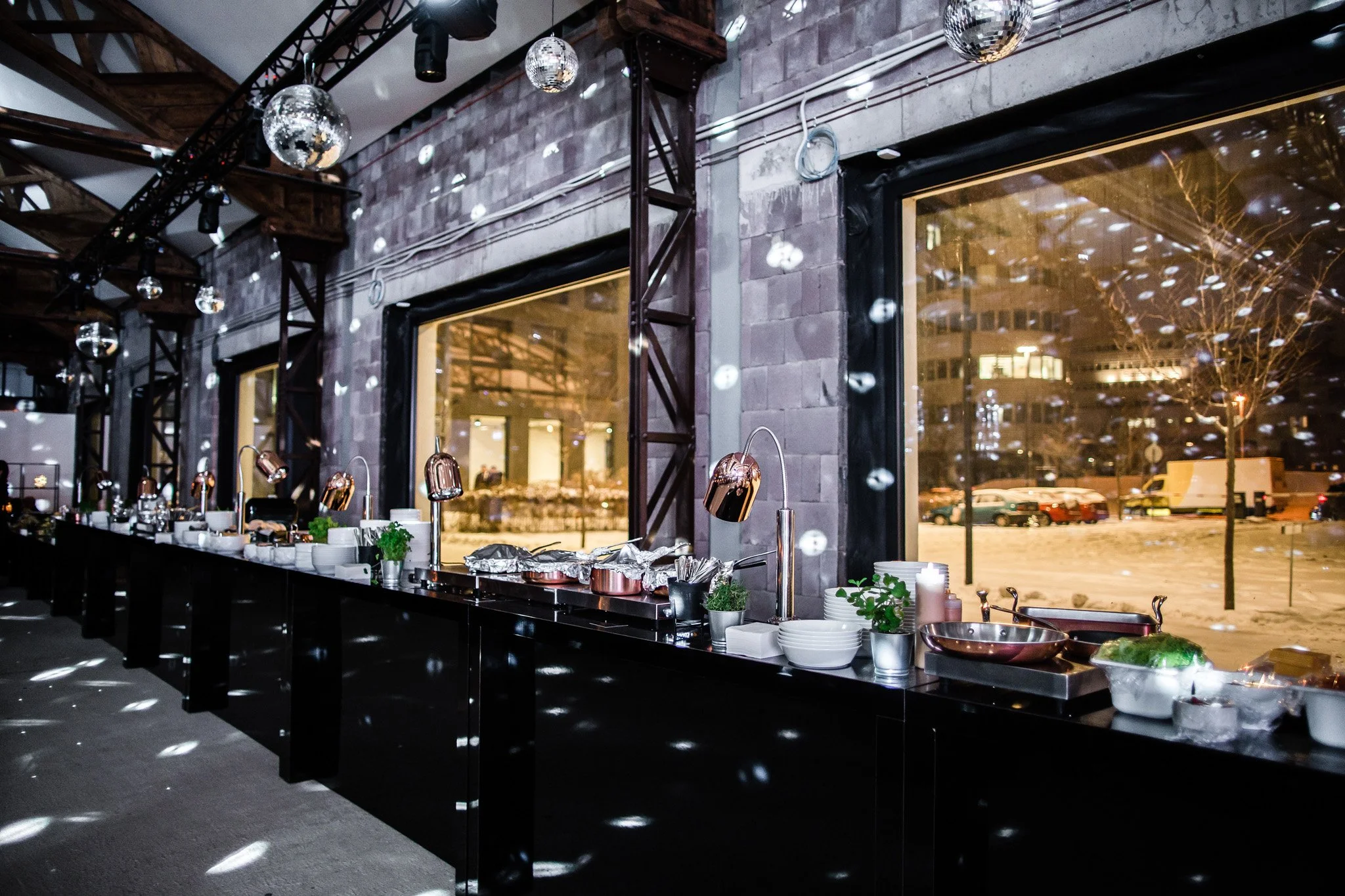 Buffet table setup with chafing dishes, plates, and decorations inside a modern venue with large windows showing a snowy outdoor scene. Catering and food photography in Zürich, Zug, Bern, Lucerne, Basel, St. Gallen and across Switzerland.